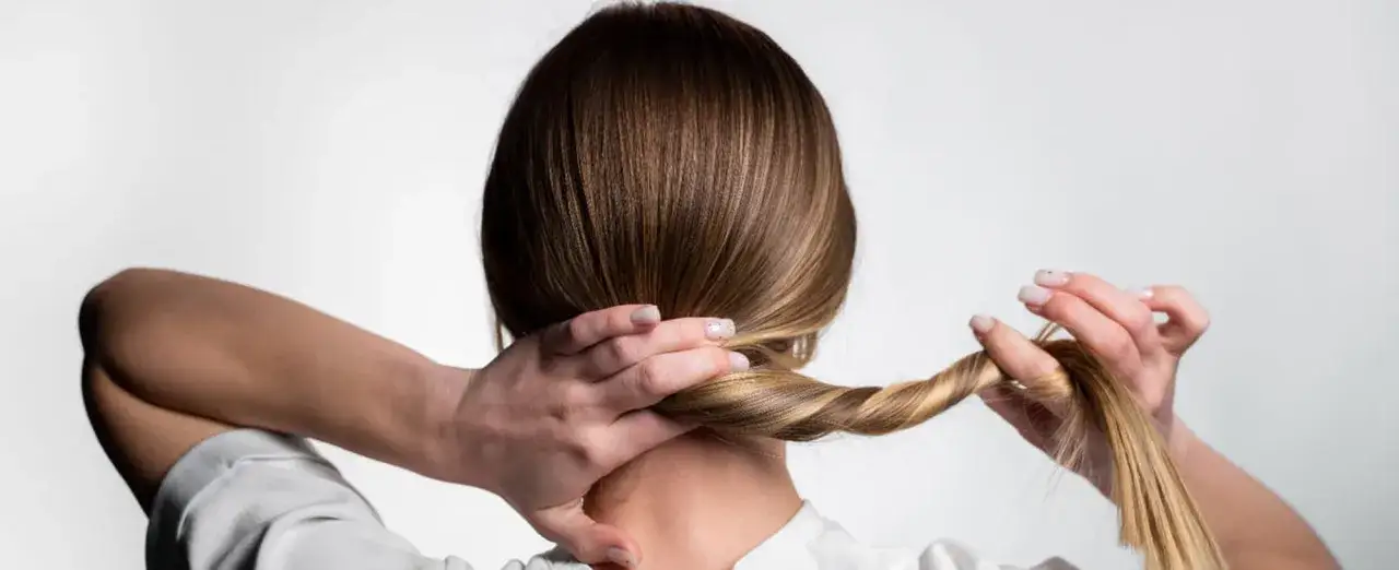 Mujer trenzando su cabello, un peinado para dormir que protege tu melena.