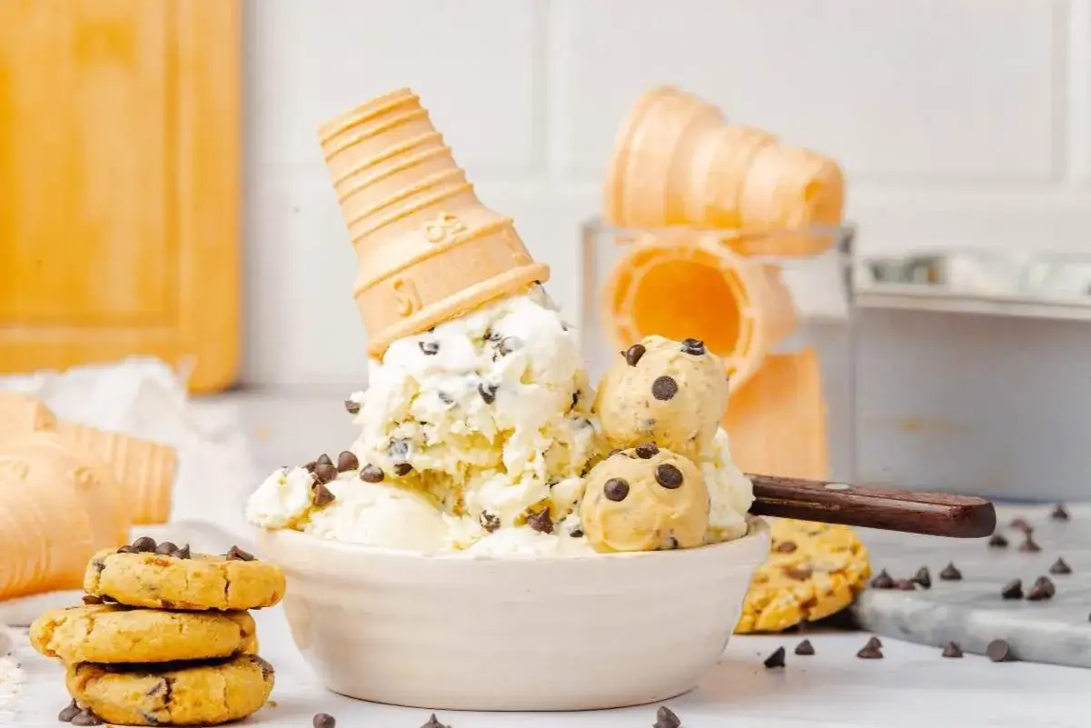 Cremiges Cookie Dough Eis selber machen: Eine Schüssel voller Eis mit Schokostückchen, Teigkugeln und einem umgedrehten Waffelhörnchen.