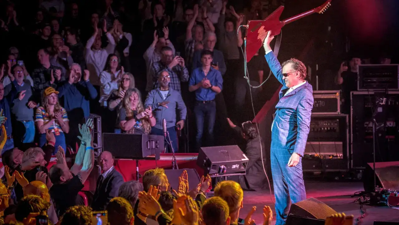 Joe Bonamassa hyllas av publiken under ett kommande evenemang. Han håller upp sin gitarr i luften.