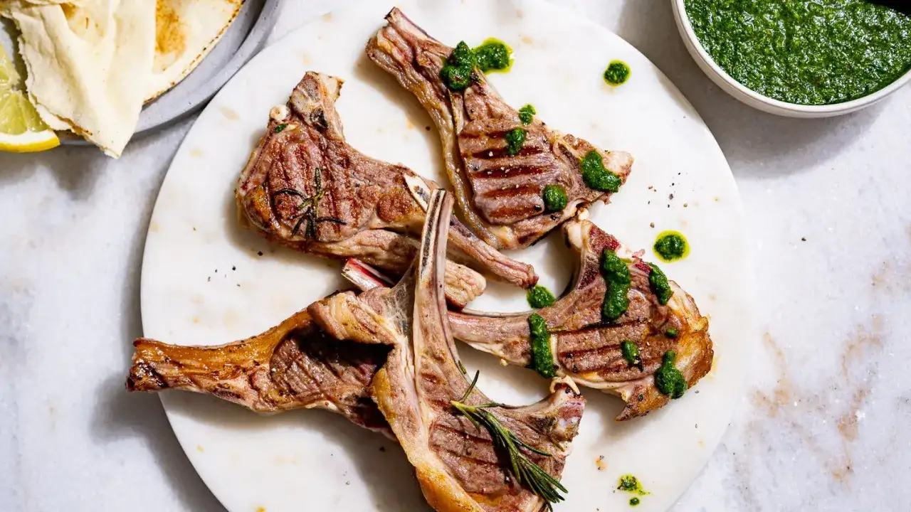 C&ocirc;telettes d'agneau grill&eacute;es au barbecue, napp&eacute;es d'une sauce verte vibrante. Un d&eacute;lice estival.