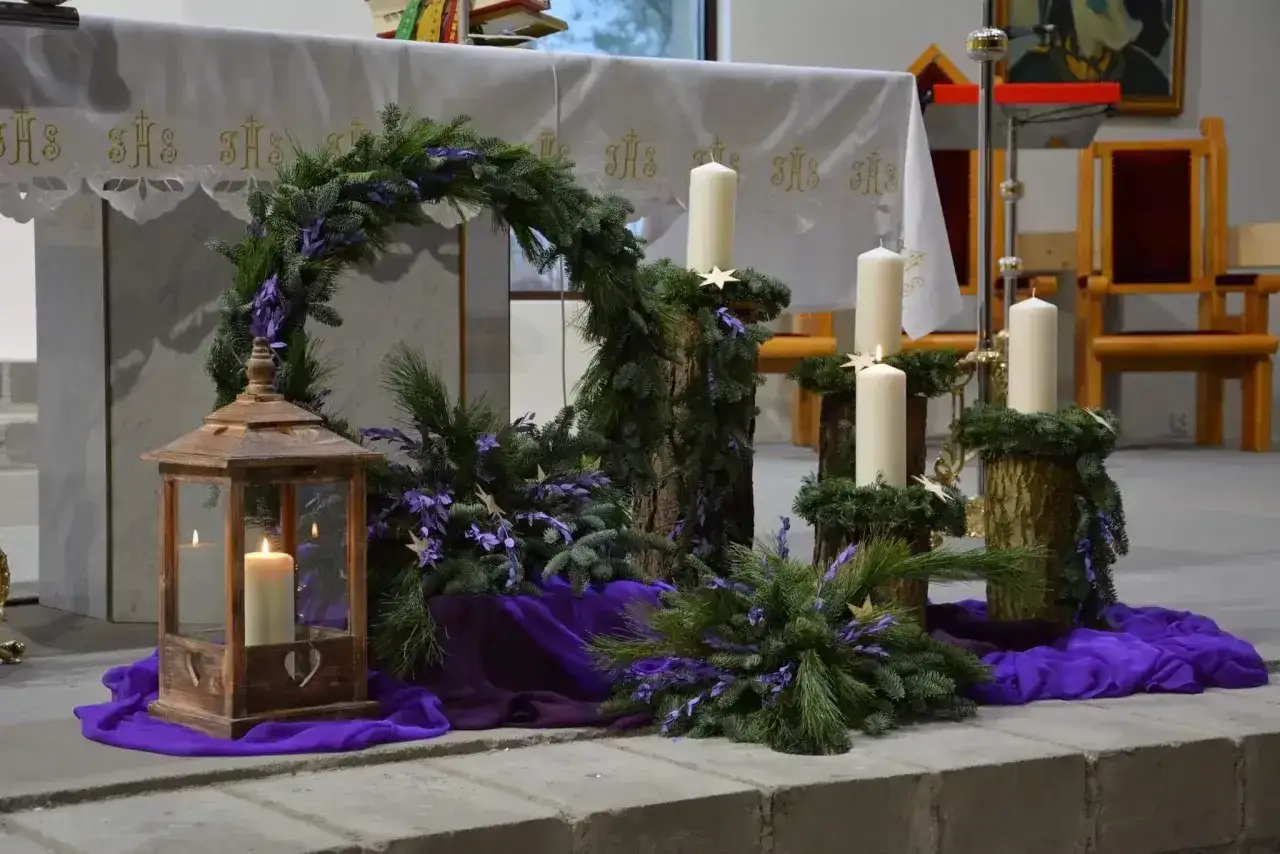 Piękny adwentowy wystrój w kościele: wieniec z gałązek, cztery świece i lampion. Dekoracje adwentowe tworzą uroczysty nastrój.