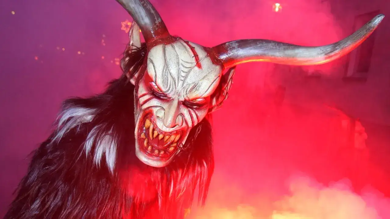 Gruselig, wie der Teufel aussieht: eine Maske mit Hörnern, spitzen Zähnen und dunklem Fell, umgeben von rotem Nebel.