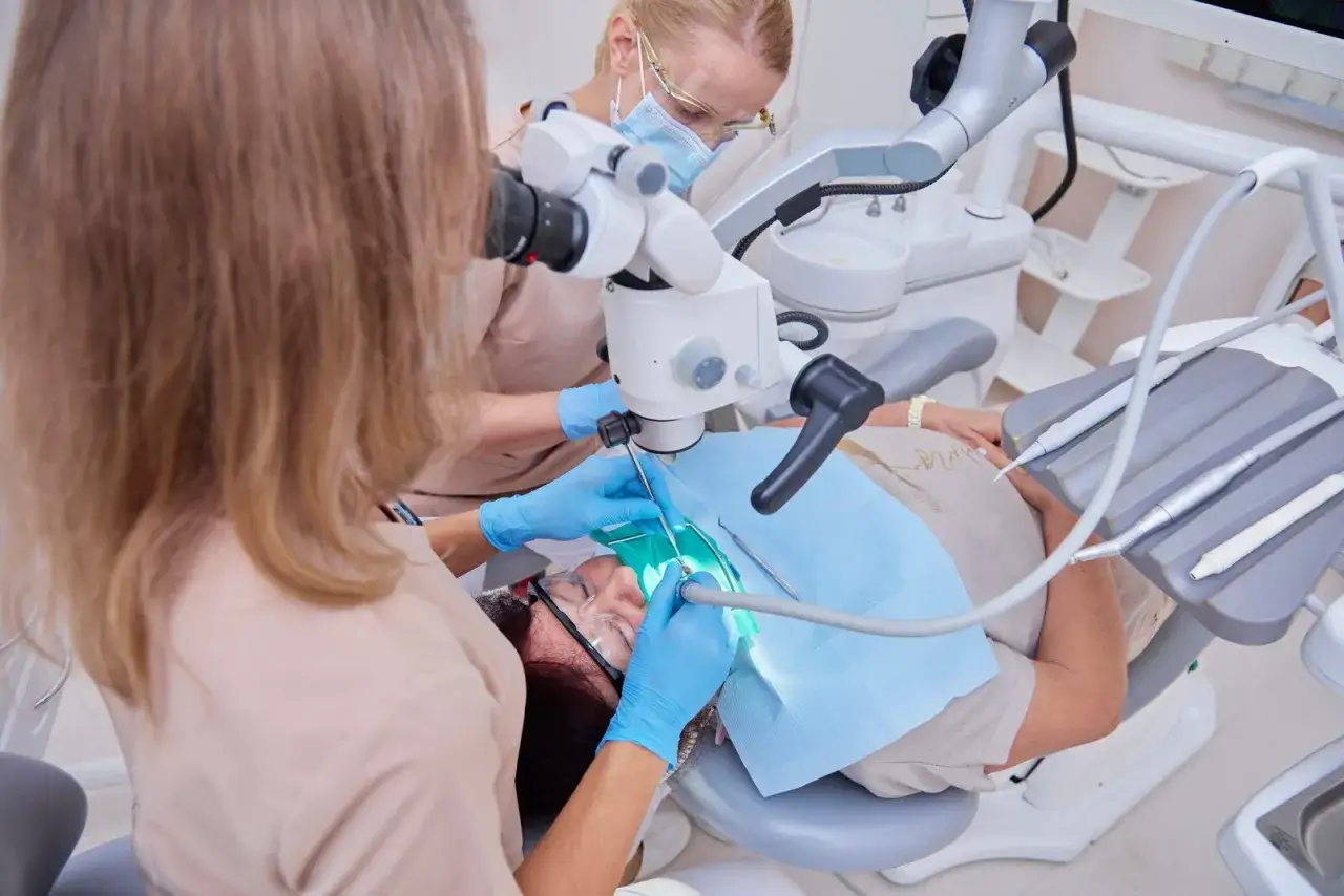 Dentystka pod mikroskopem wykonuje zabieg leczenia paradontozy. Pacjentka w fotelu dentystycznym.