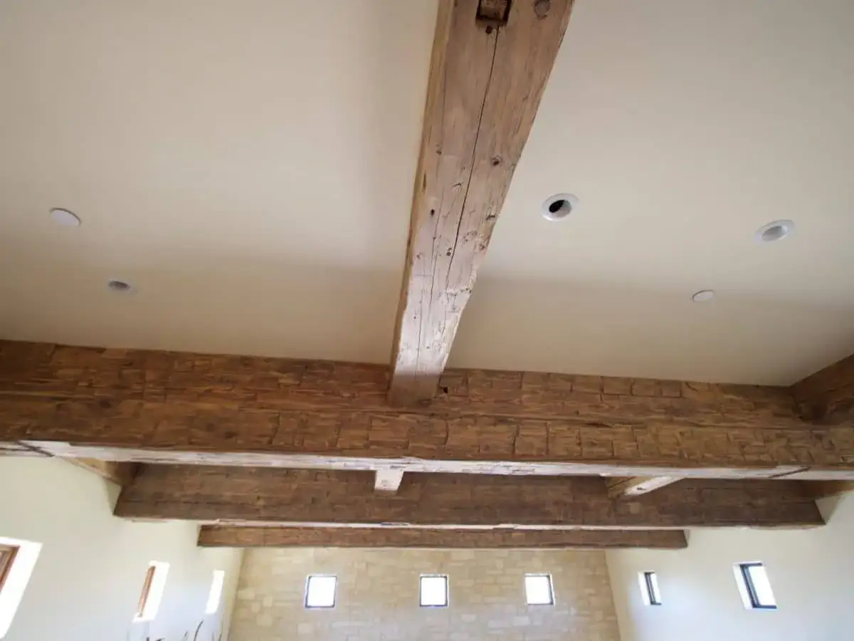 Poutres apparentes en bois cir&eacute;, patin&eacute;es par le temps, soutenant un plafond blanc avec des spots encastr&eacute;s.