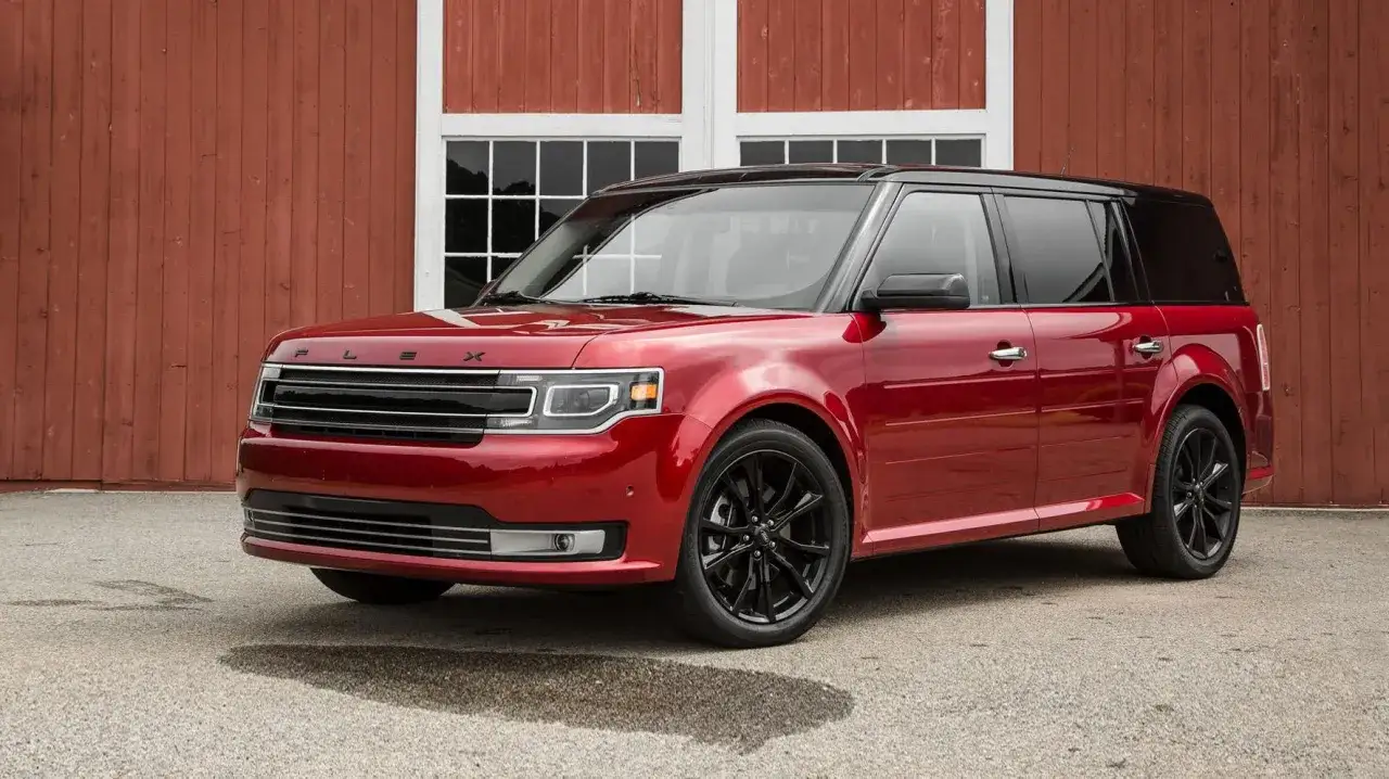Czerwony Ford Flex z czarnym dachem i czarnymi felgami stoi przed czerwoną stodołą z białymi oknami.