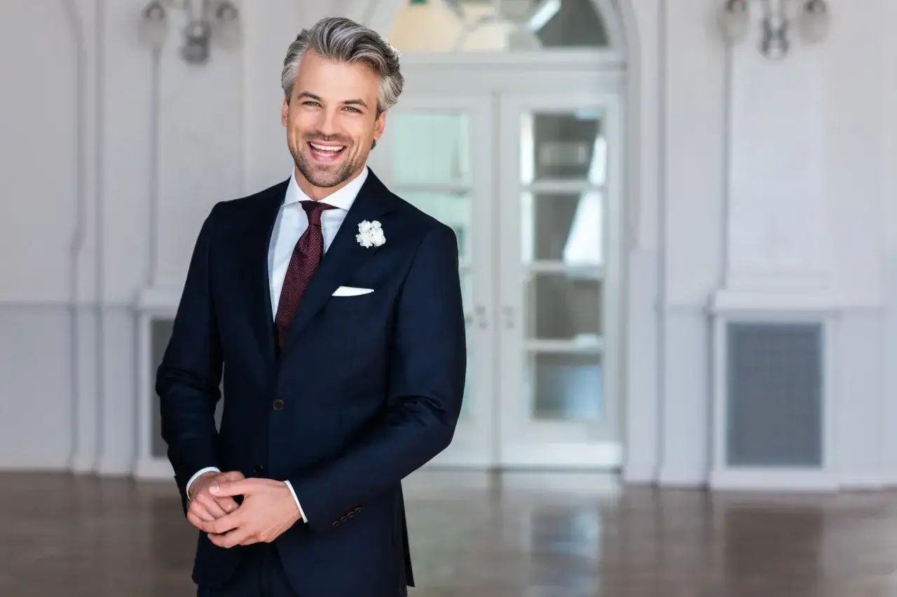 Elegancki mężczyzna w granatowym garniturze, białej koszuli i bordowym krawacie. Idealna stylizacja, kt&oacute;ra odpowiada na pytanie: jaka koszula do granatowego garnituru.