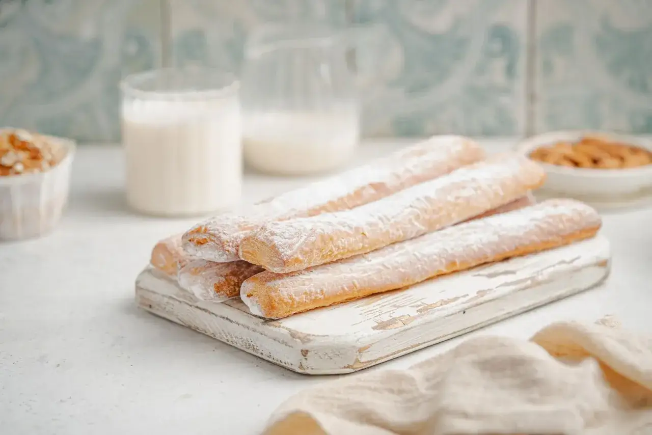 Dulces t&iacute;picos de Valencia: palitos dorados espolvoreados con az&uacute;car glas sobre tabla de madera.