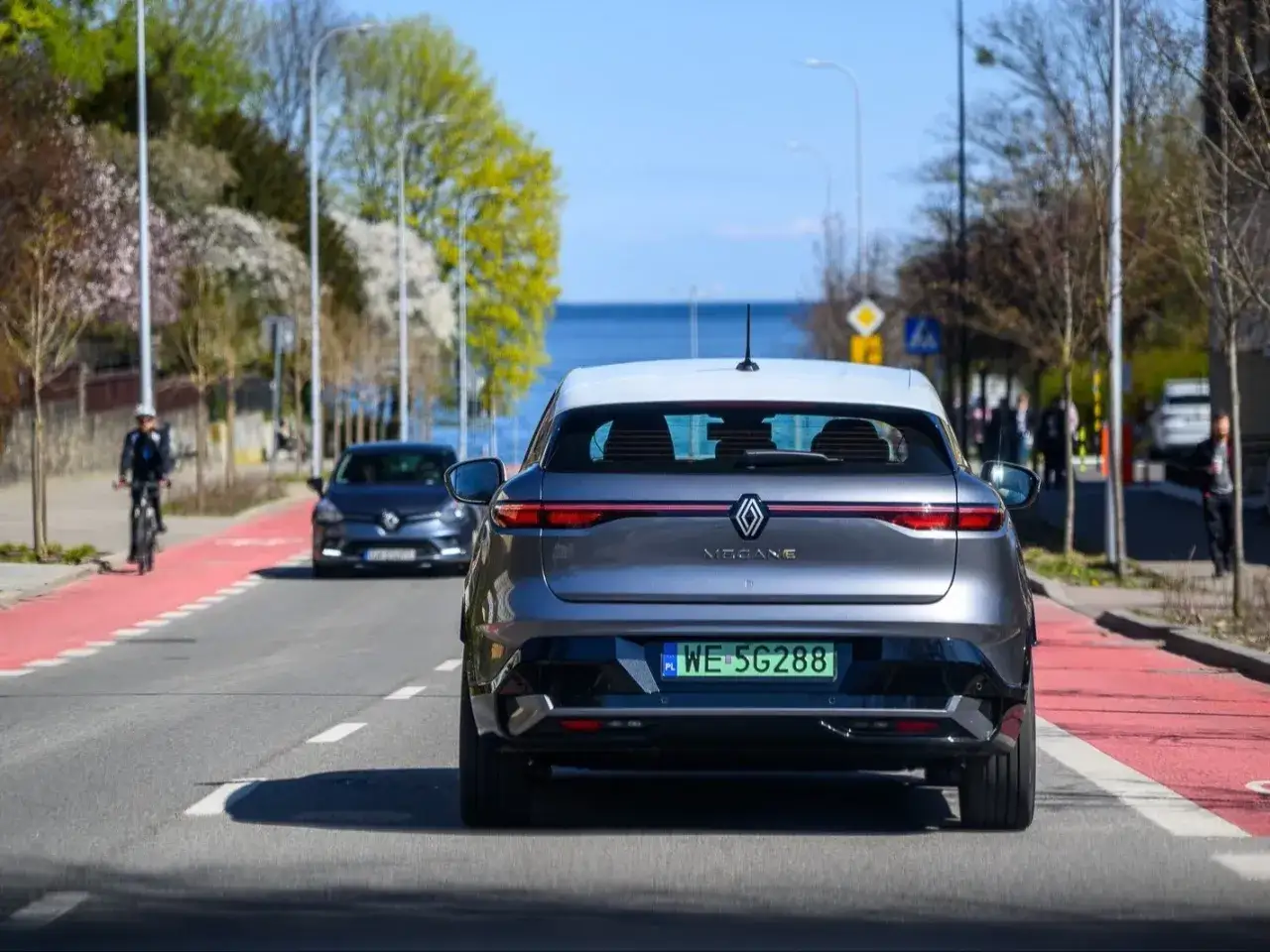 Szary Renault Megane na drodze, w tle widać rowerzystę i morze. Miła jazda samochodem w słoneczny dzień.
