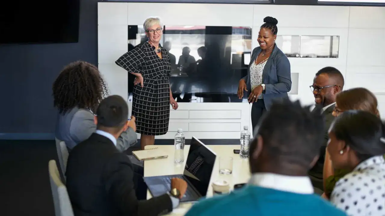 Two women present to a diverse group, illustrating behavioral theory in action.