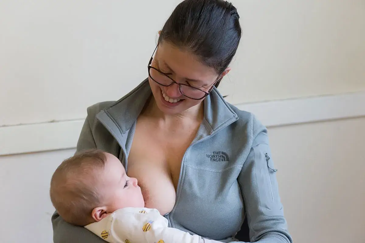 Madre sorride mentre allatta il suo neonato. Il piccolo, con una tutina a api, sembra tranquillo, nonostante il reflusso neonato allattato al seno sia una preoccupazione comune.