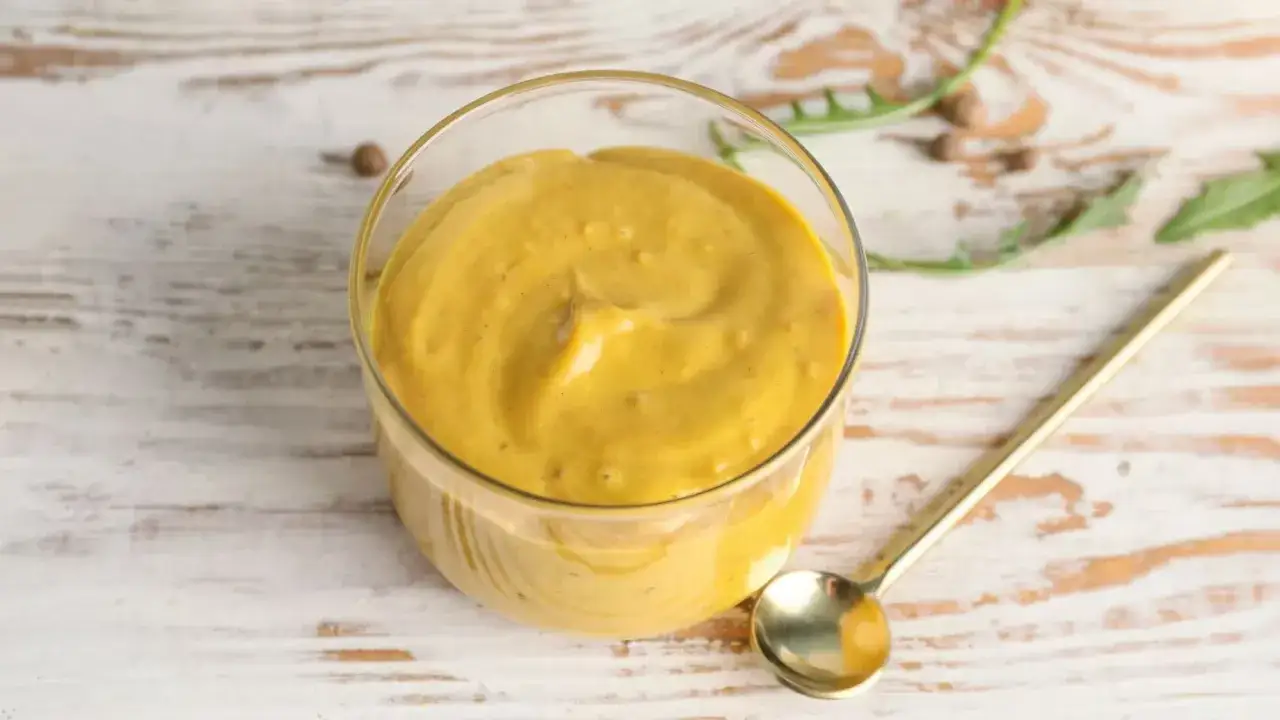 Sauce raclette facile dans un bol en verre, avec une cuillère dorée à côté. Parfait pour accompagner votre fromage fondu.