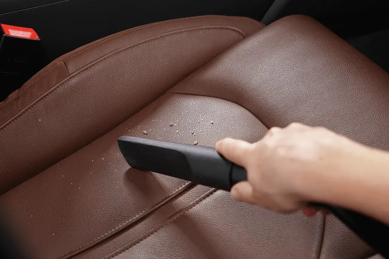Hand saugt Krümel vom braunen Leder-Autositz. So einfach ist leder reinigen.