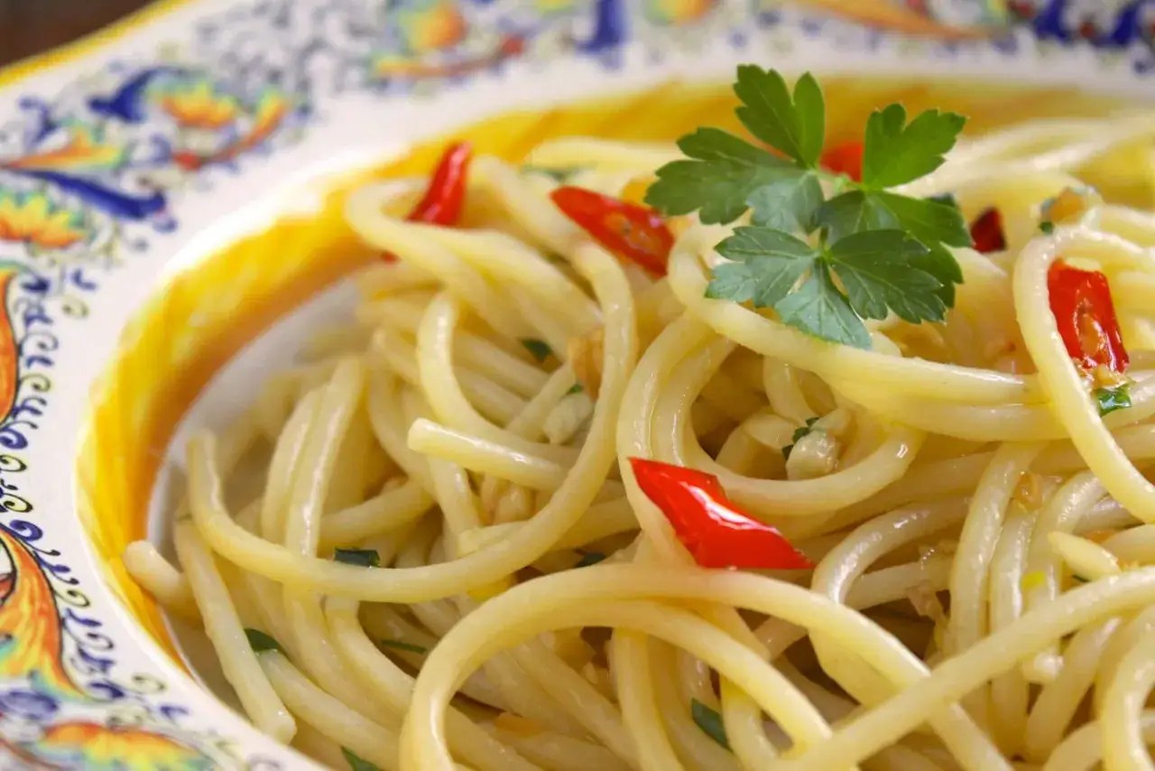 Un plato de espagueti aglio olio peperoncino, con trozos de chile rojo y perejil fresco, servido en una vajilla decorada.