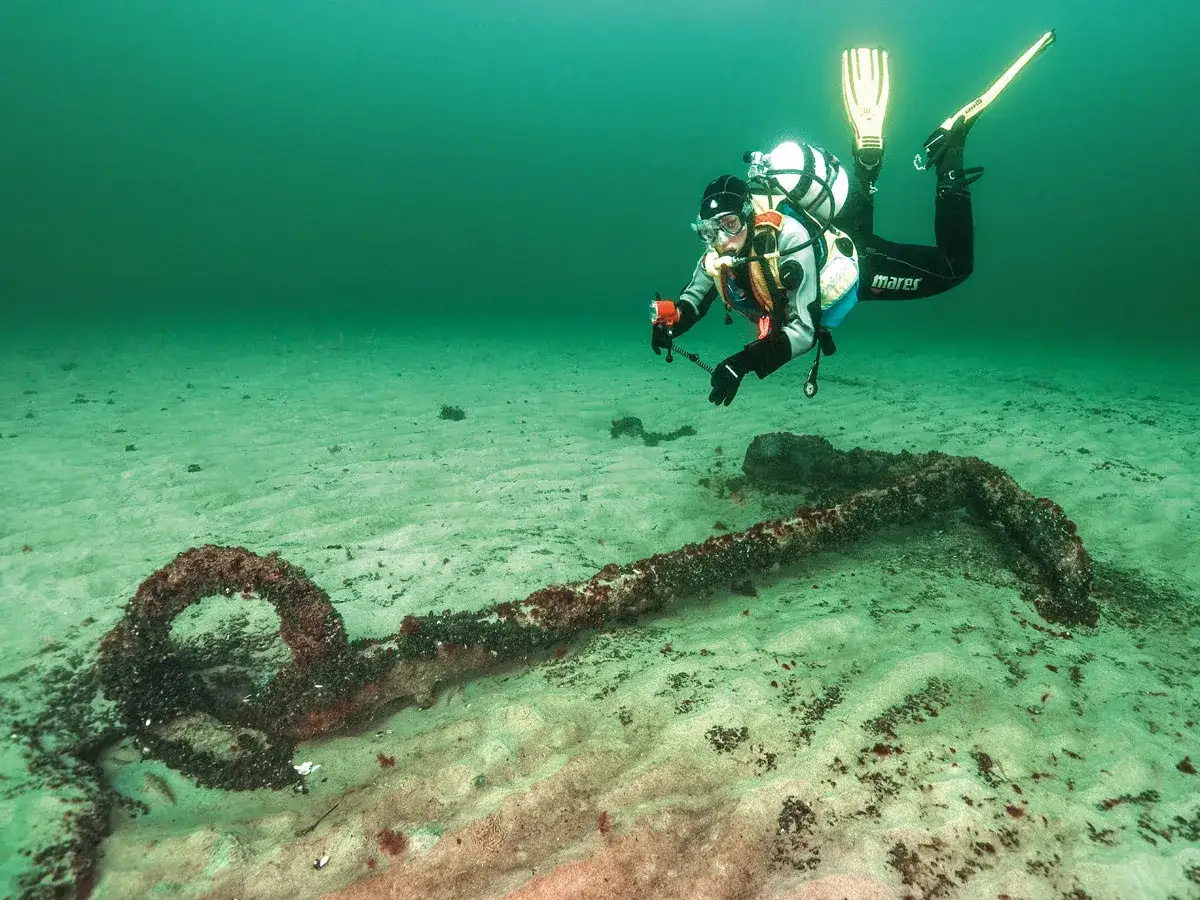 Taucher erkundet ein altes Ankerwrack auf dem sandigen Grund der Ostsee.