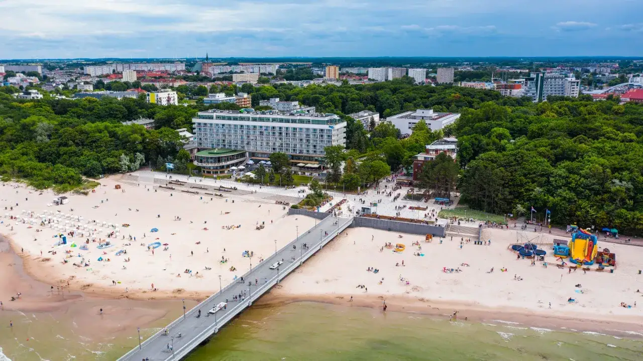 Kołobrzeg atrakcje dla dzieci: plaża z dmuchanymi zjeżdżalniami i trampolinami, molo, hotel i zielone tereny.