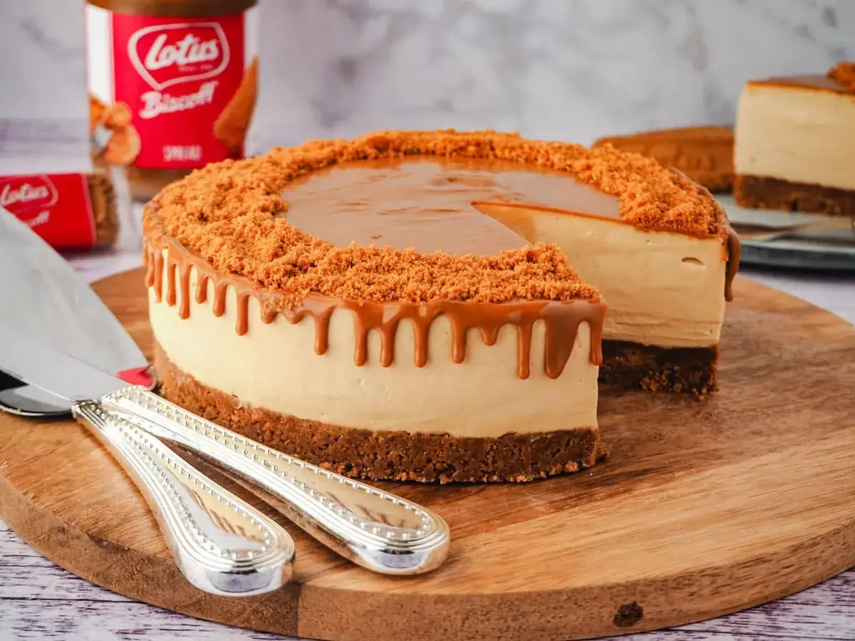 Ein k&ouml;stlicher Lotus Cheesecake mit Karamell-Drip und Keksbr&ouml;seln. Ein St&uuml;ck ist bereits angeschnitten.