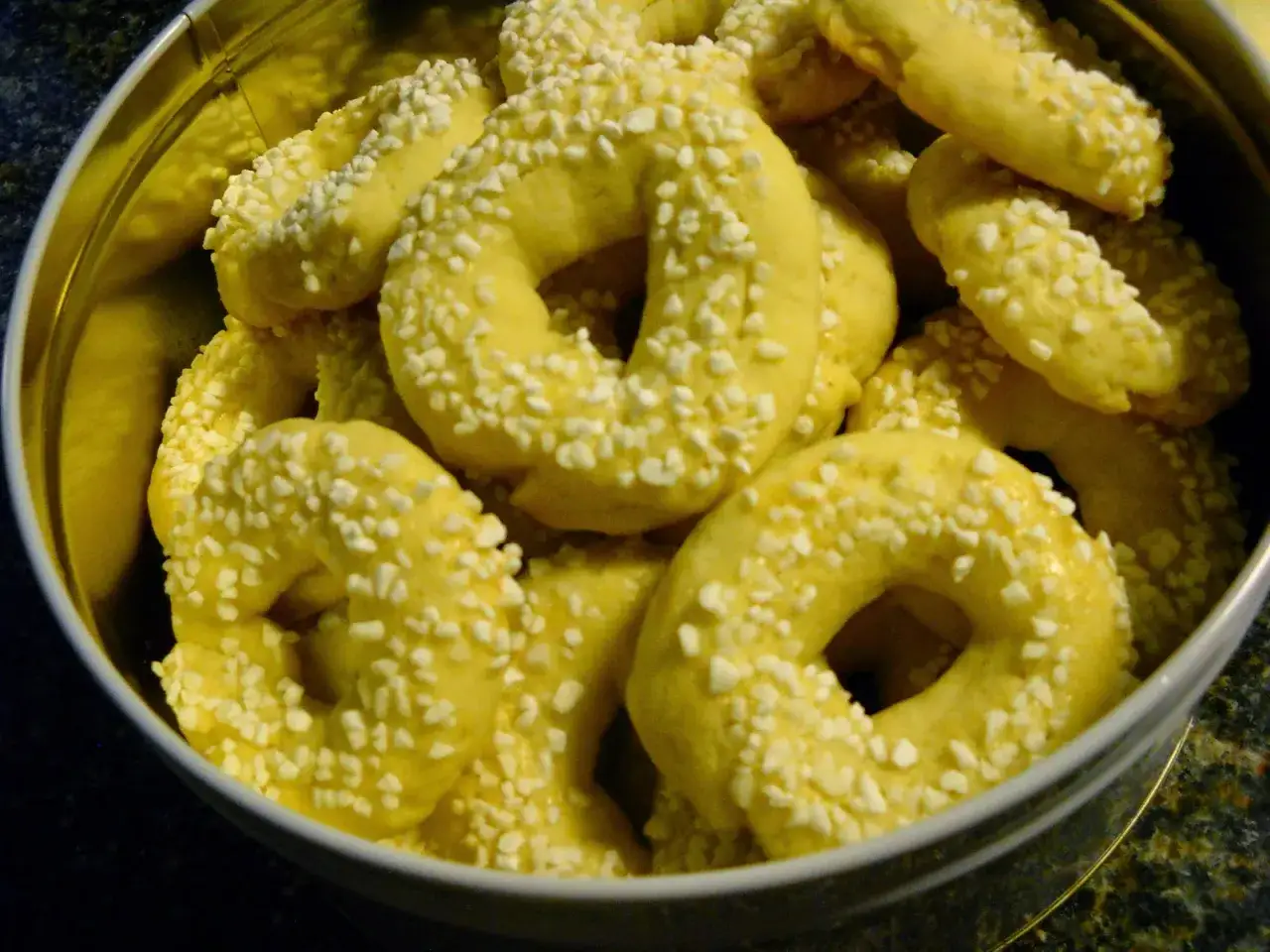 En burk fylld med gyllene kringlor med bakpulver, str&ouml;sslade med sm&aring; vita bitar.