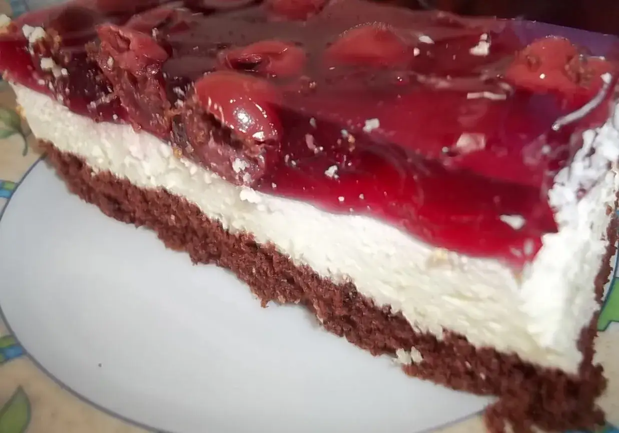 Ciemny biszkopt z wiśniami i bitą śmietaną, oblany galaretką. Pyszny deser na talerzu.