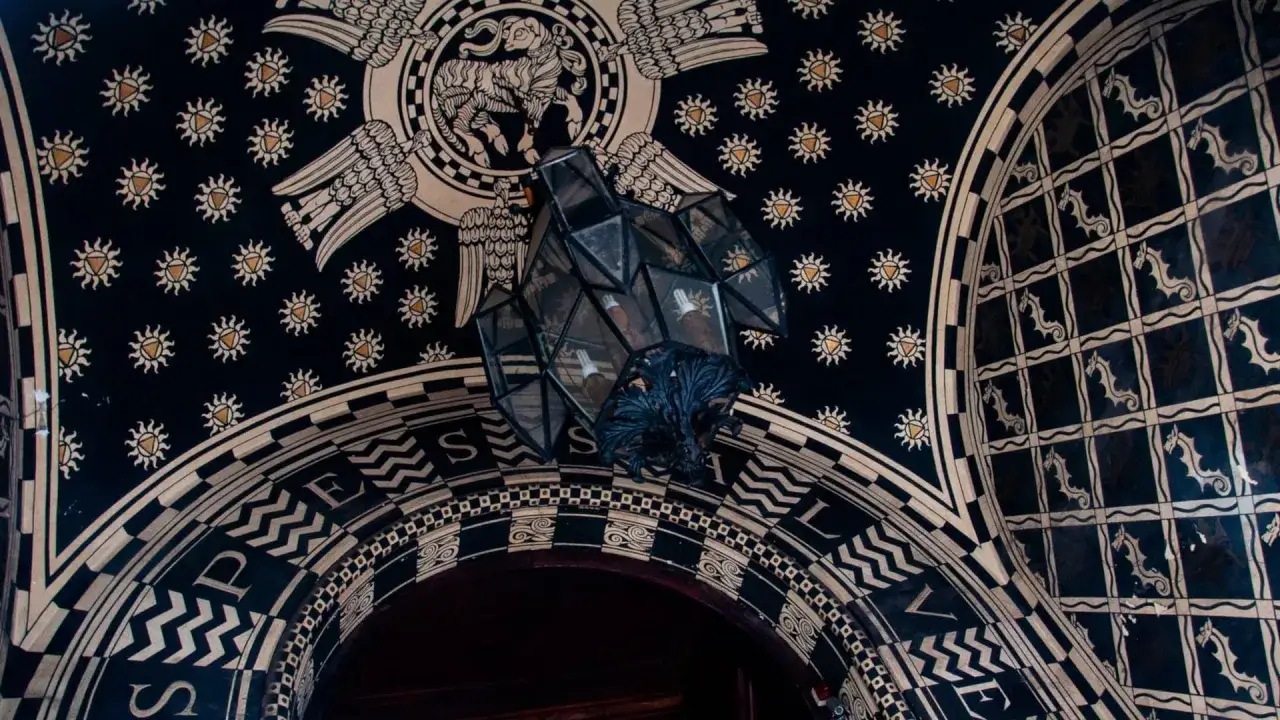 Interni del Quartiere Coppedè: soffitto decorato con simboli celesti, creature mitologiche e un lampadario geometrico.