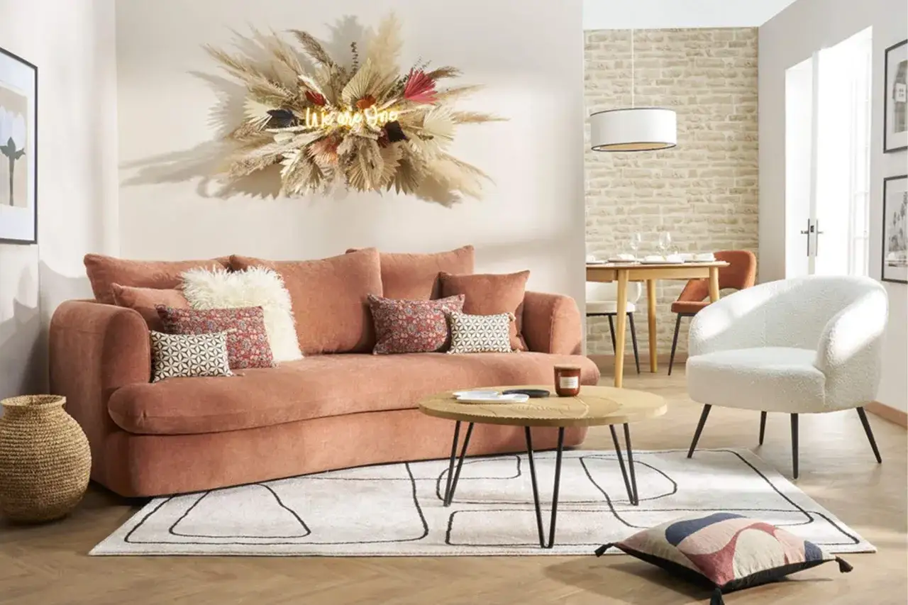 Canapé moelleux couleur terracotta, coussins décoratifs, table basse ronde, tapis graphique et fauteuil blanc bouclé. Une ambiance chaleureuse.