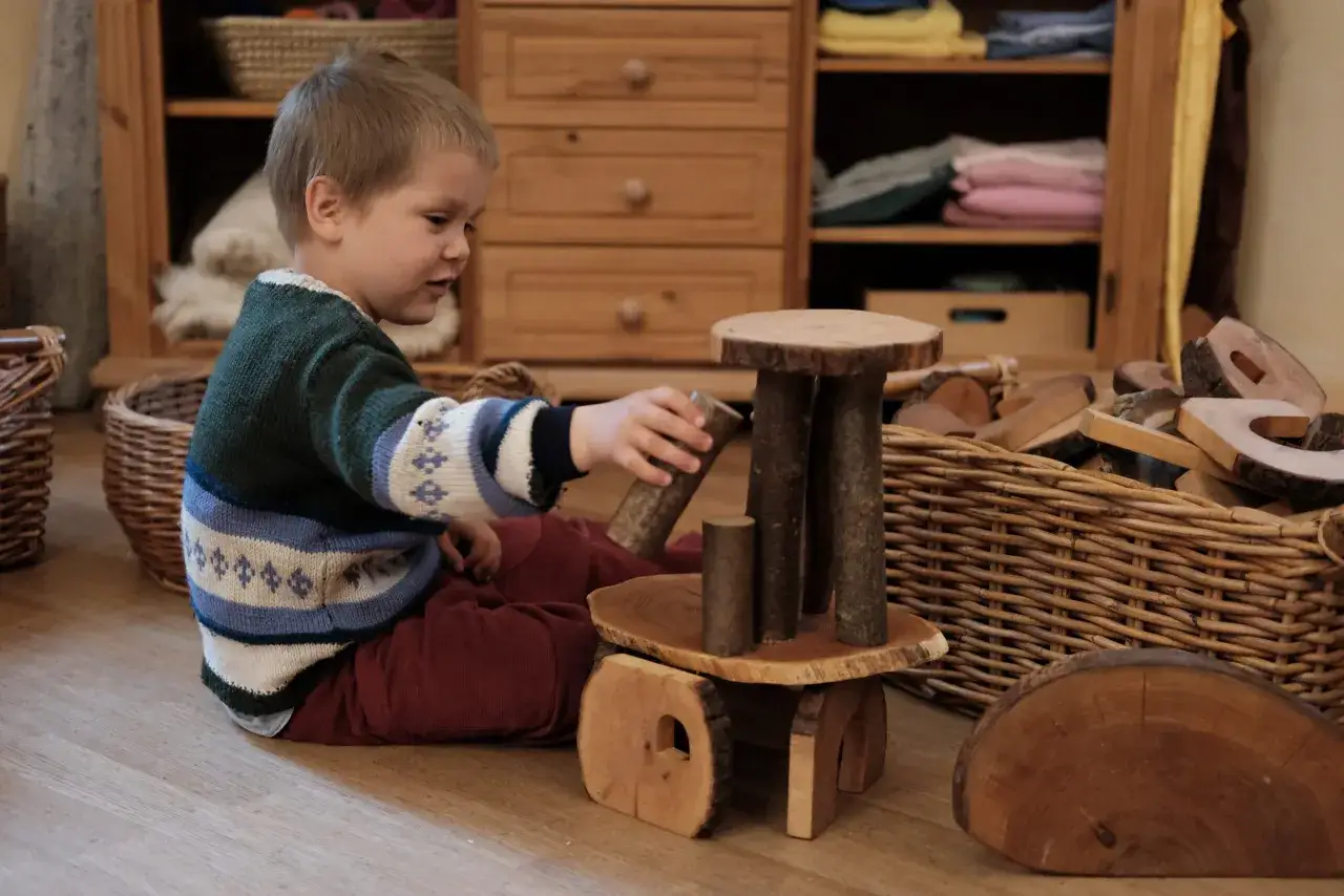 Ein Junge spielt mit Holzbausteinen, die das Waldorf Konzept widerspiegeln. Natürliche Materialien fördern Kreativität und Fantasie.