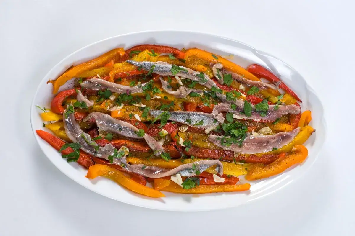 Peperoni sott'olio con acciughe e capperi, un antipasto colorato e saporito, guarnito con prezzemolo fresco.