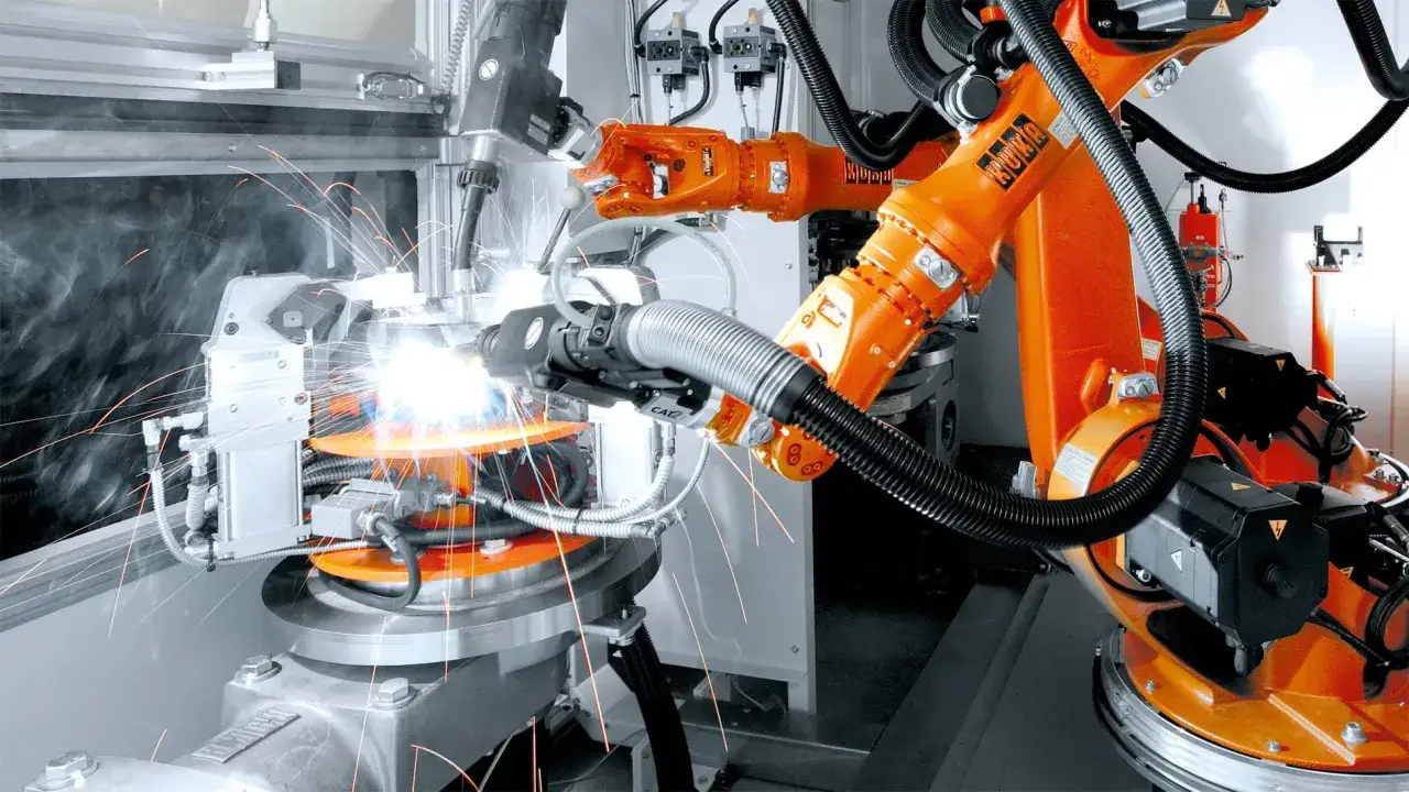 Brazos robóticos naranjas realizan soldadura por arco eléctrico, generando chispas brillantes en una fábrica automatizada.