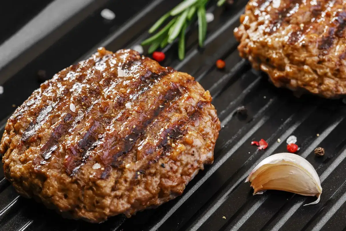 Soczyste burgery z grilla, doprawione solą i pieprzem, z gałązką rozmarynu i ząbkiem czosnku.
