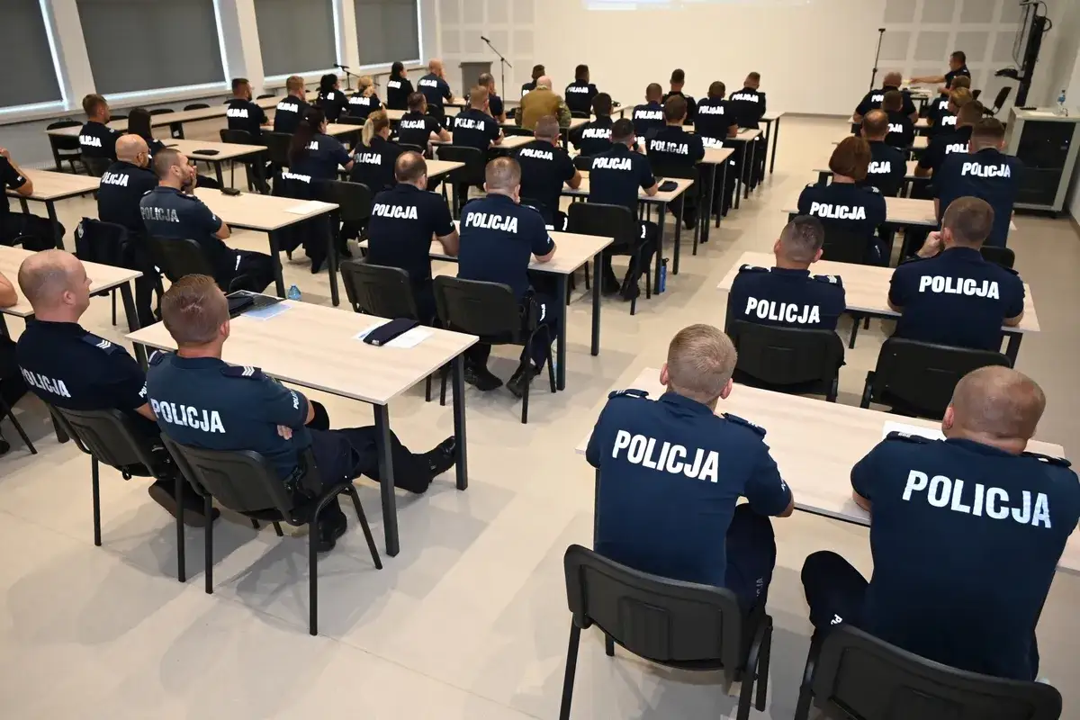 Policjanci na szkoleniu, uczą się jak zostać podkomisarzem policji. W sali wykładowej siedzą w ławkach, słuchając wykładu.