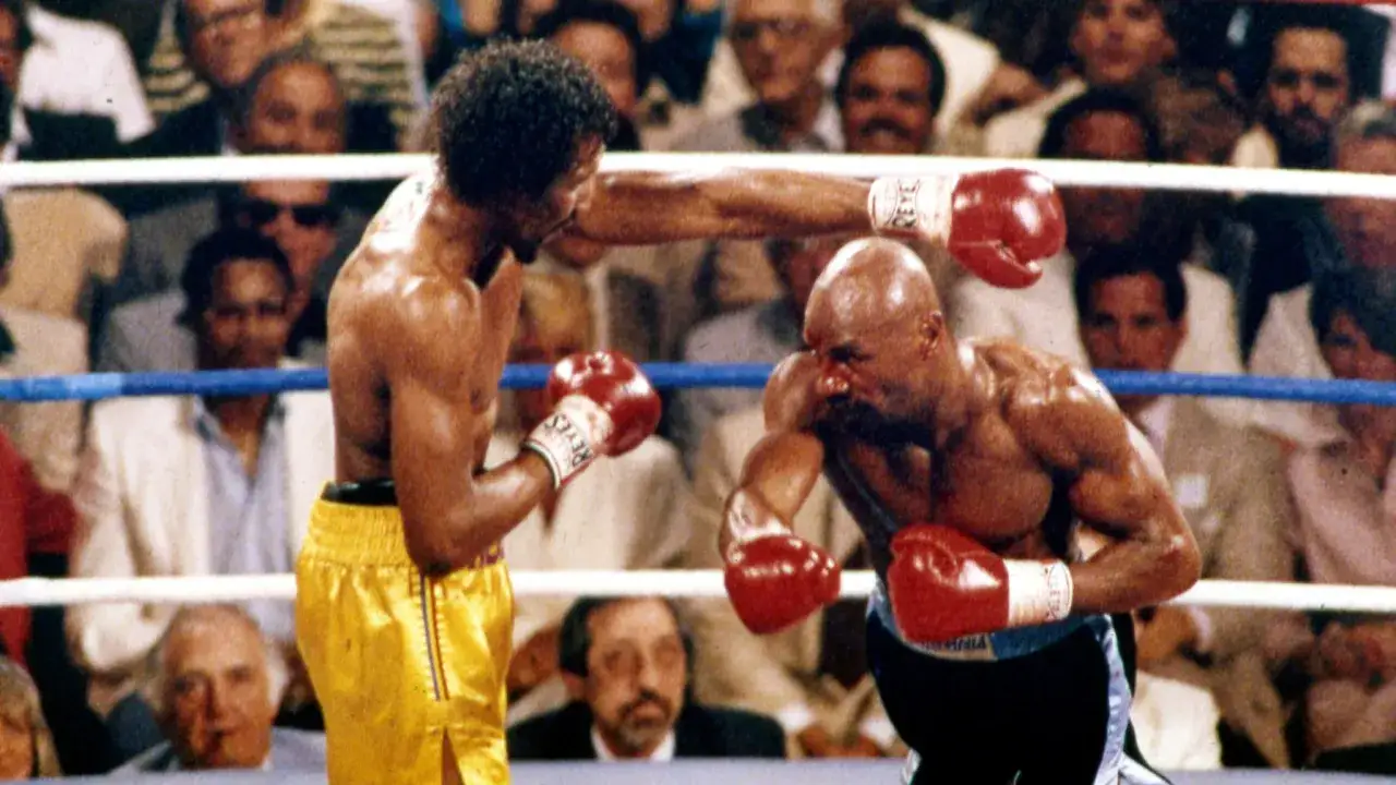 The epic Hearns vs Hagler boxing match. Hearns lands a punch on Hagler's face as the crowd watches intently.