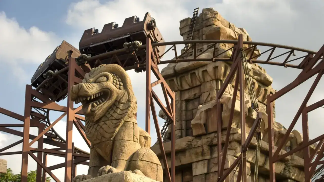 El tren de la monta&ntilde;a rusa disneyland paris se desliza junto a una estatua de le&oacute;n de piedra y ruinas antiguas.