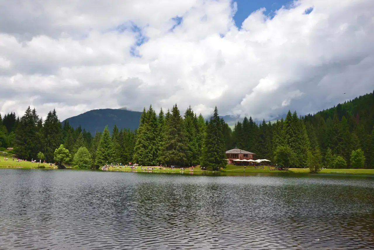 Il lago dei caprioli, circondato da fitti boschi di abeti, accoglie visitatori che si rilassano sull'erba e un rifugio con tavoli all'aperto.