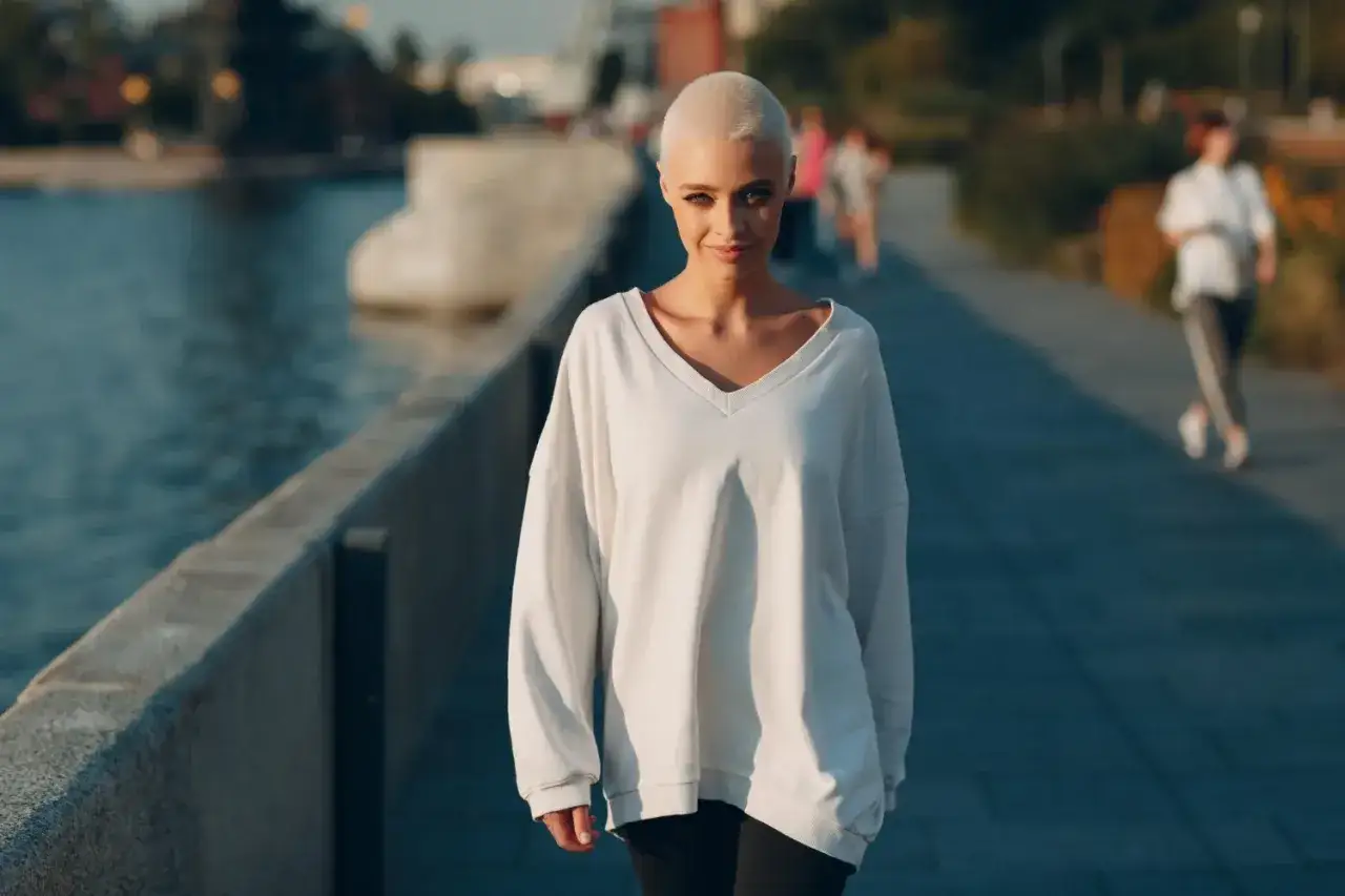 Kobieta z kr&oacute;tkimi blond włosami w białej bluzie w stylu oversize idzie wzdłuż nabrzeża.