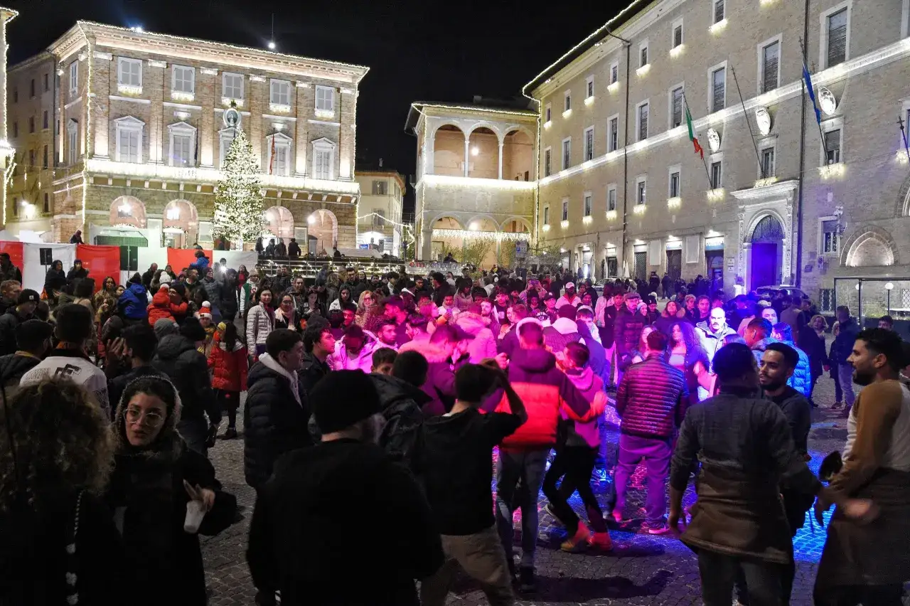 Folla festante in piazza per il capodanno Civitanova Marche, con un grande albero illuminato e palazzi addobbati.