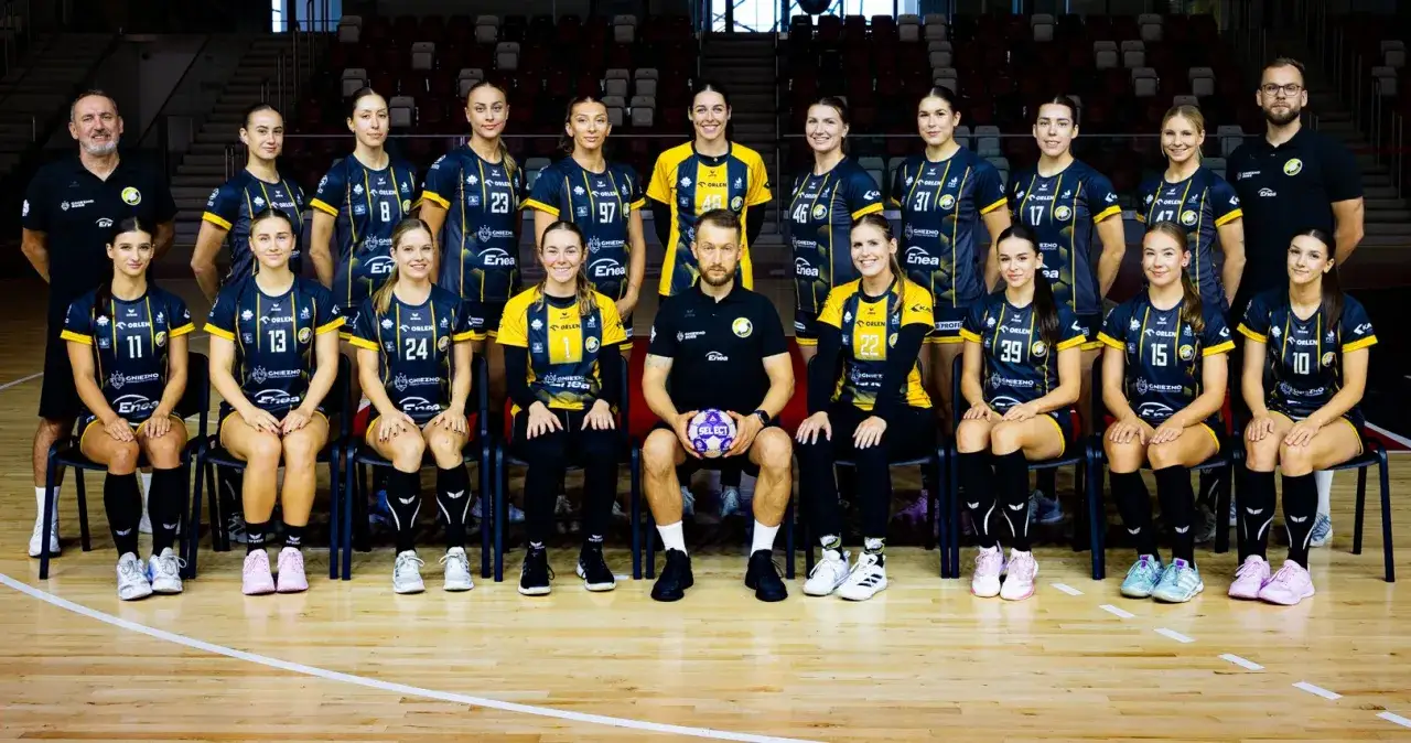 Drużyna MKS Gniezno piłka ręczna pozuje do zdjęcia. Zawodniczki w strojach z numerami i trenerzy gotowi do gry.