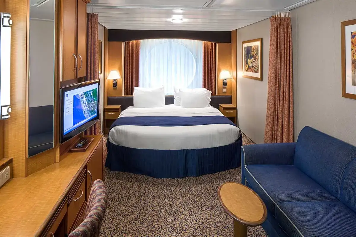 Accogliente cabina garantita Costa Crociere con letto matrimoniale, divano blu, TV e oblò circolare.
