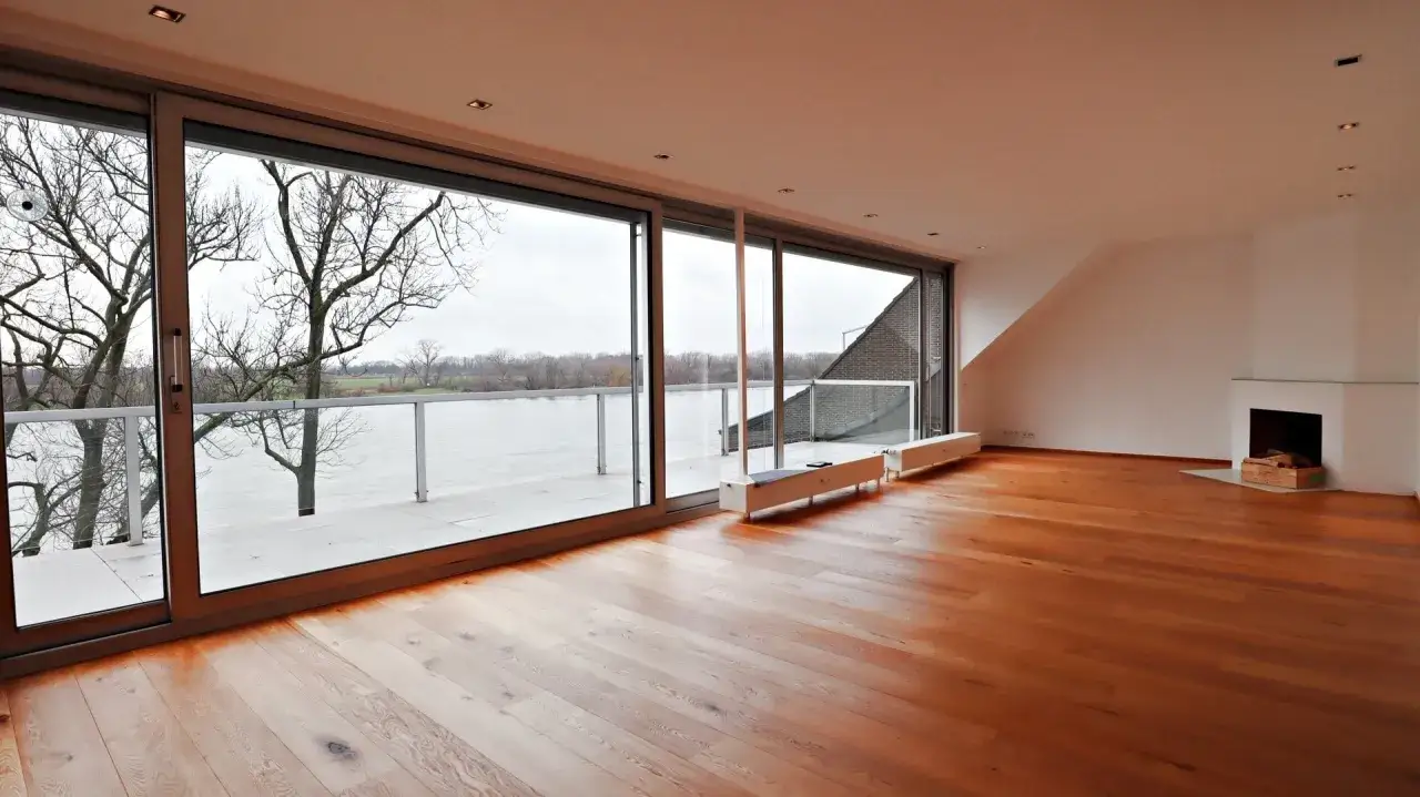 Großzügiges Wohnzimmer mit Parkettboden, Kamin und Panoramablick auf den Rhein. Hier könnte Ihre Traumimmobilie in Wittlaer liegen, die Immobilienpreise sind attraktiv.