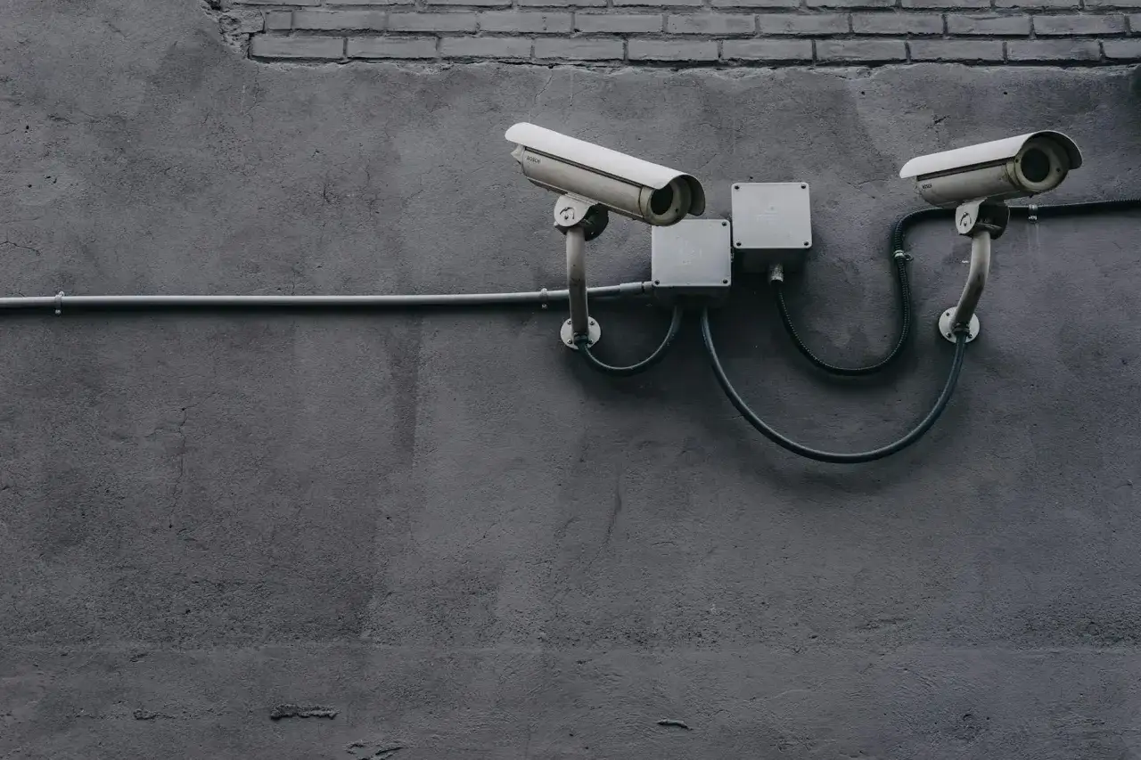 Dwa kamery monitoringu na szarej ścianie. System zapewnia udostępnianie nagrań z monitoringu, dbając o bezpieczeństwo.