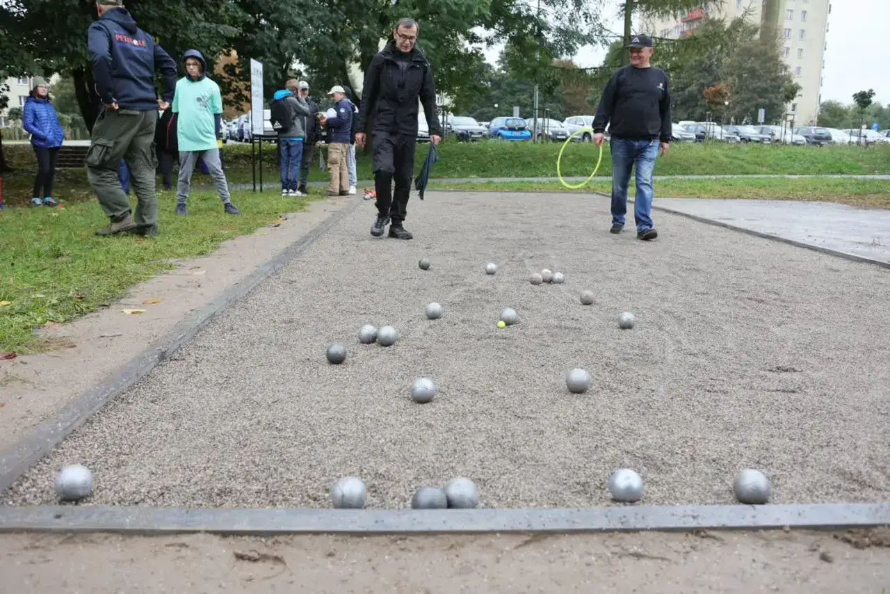 Ludzie grają w bule, rzucając metalowe kule na żwirowisko. Zasady gry w bule są proste: zbliżyć się do małej kulki.