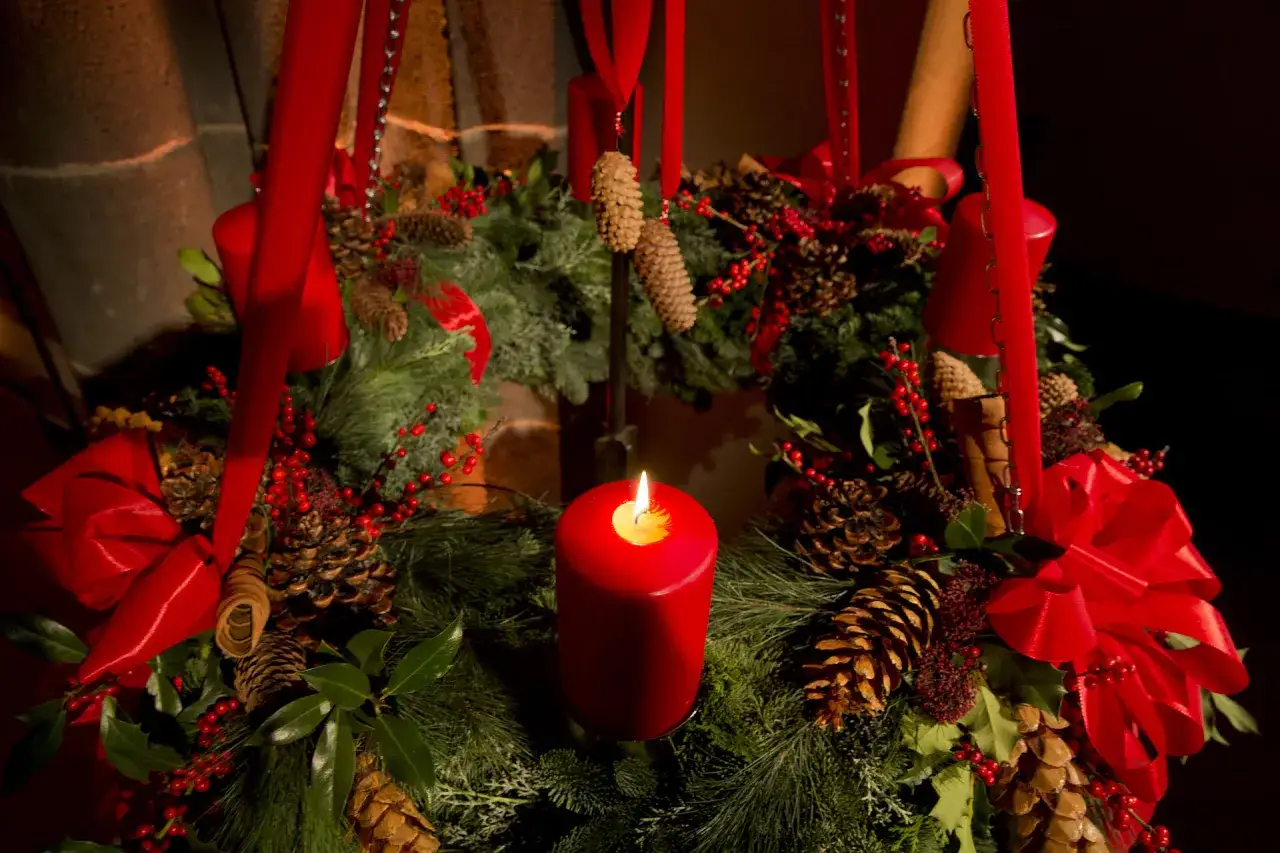 Adventskranz mit brennender Kerze, Tannenzweigen, Zapfen und roten Bändern. Stimmungsvoller Hintergrund Adventszeit.