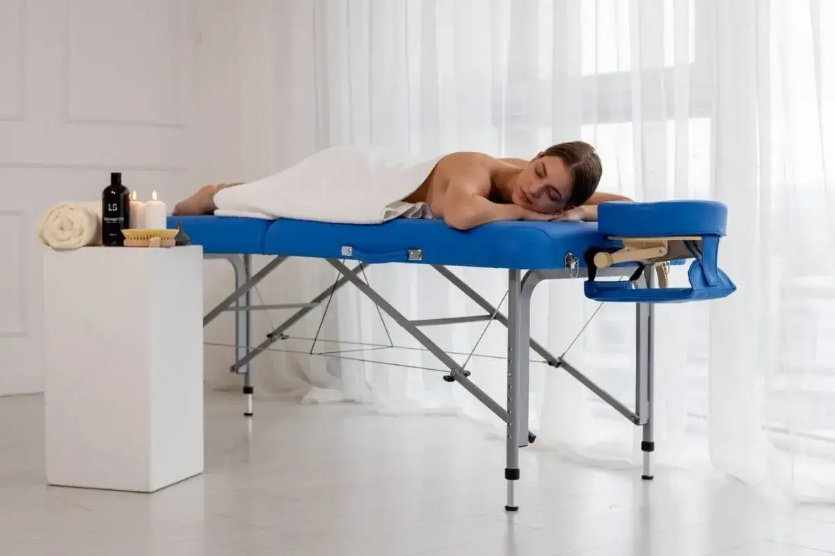 Kobieta leży na masażowym łóżku, przykryta białym ręcznikiem. Czy na masażu trzeba się rozebrać? Zazwyczaj tak, aby terapeuta miał dostęp do skóry.