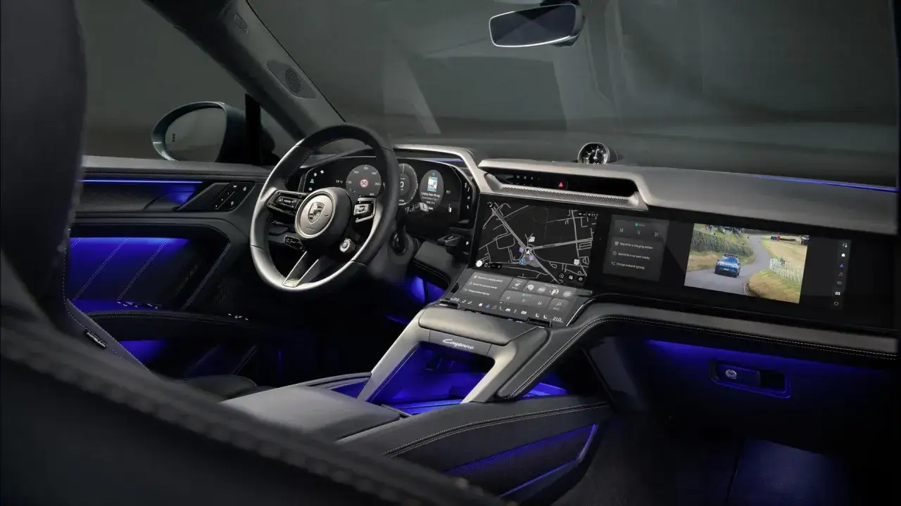 Wnętrze Porsche Cayenne 2025 z niebieskim podświetleniem ambientowym, dużym ekranem dotykowym z nawigacją i widokiem z kamery.