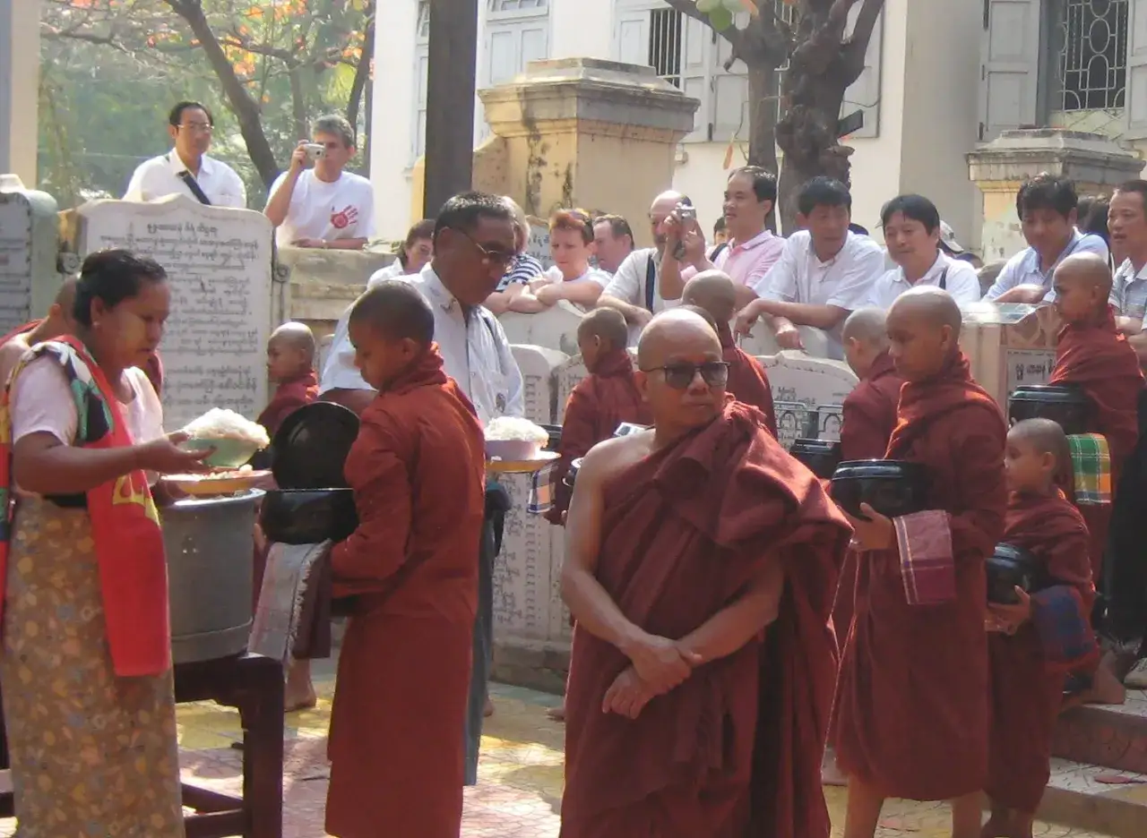 M&ouml;nche in safranfarbenen Roben erhalten Spenden. Einblicke, wie leben Buddhisten im Alltag, mit Opfergaben und Gebeten.