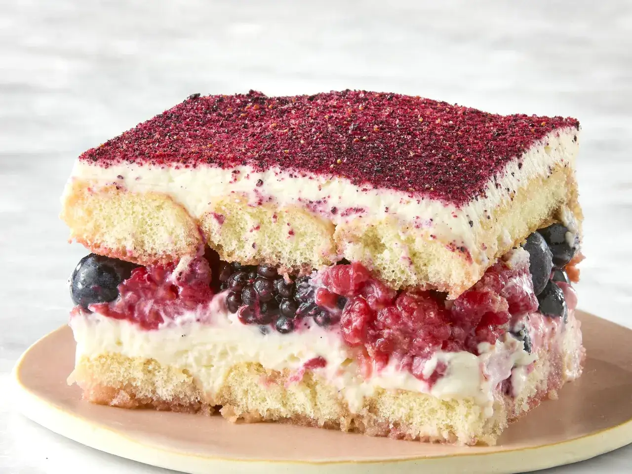 Tranche de tiramisu aux fruits rouges et myrtilles, saupoudr&eacute;e de poudre de fruits.