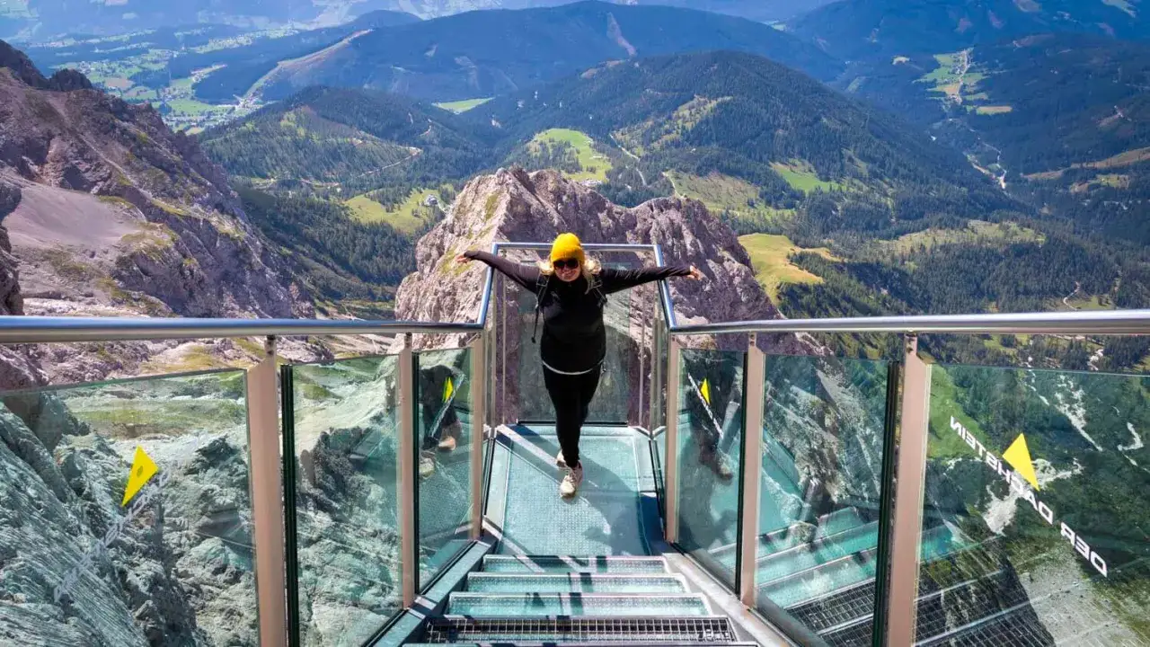 Frau auf der Aussichtsplattform der Dachstein Sonnenrunde, mit Armen ausgebreitet, genie&szlig;t den atemberaubenden Blick auf die Alpen.