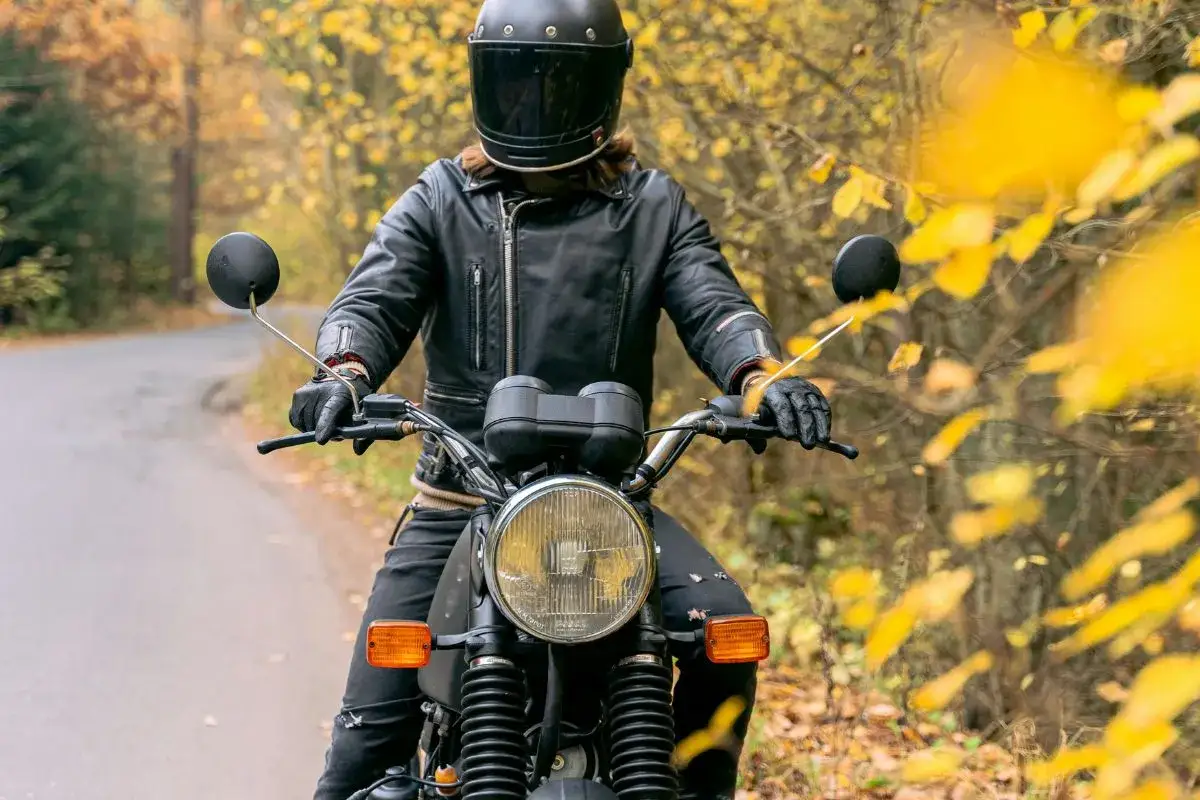 En person i läderjacka och hjälm kör motorcykel på en väg kantad av höstfärger. Känslan av frihet och a1 motorcykel hastighet infinner sig.