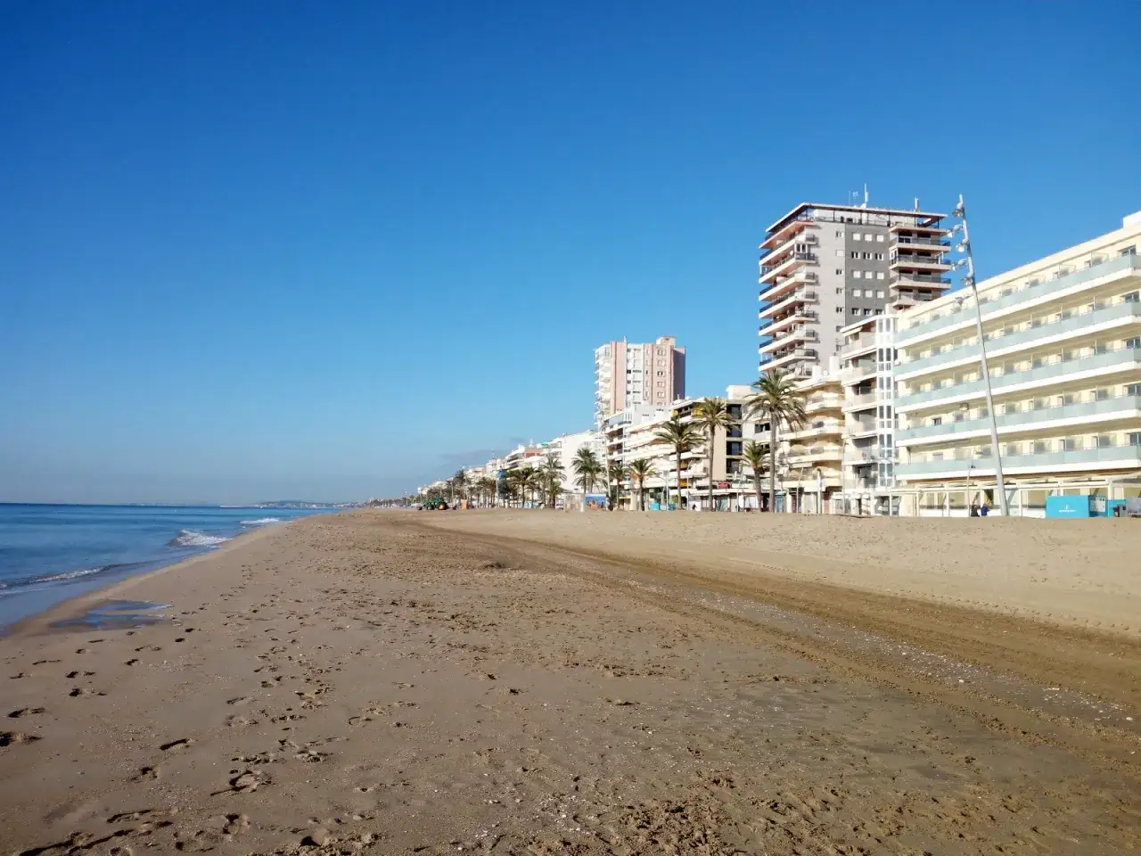 Strandpromenade in Calafell, Spanien, mit hohen Geb&auml;uden und Palmen am Horizont.