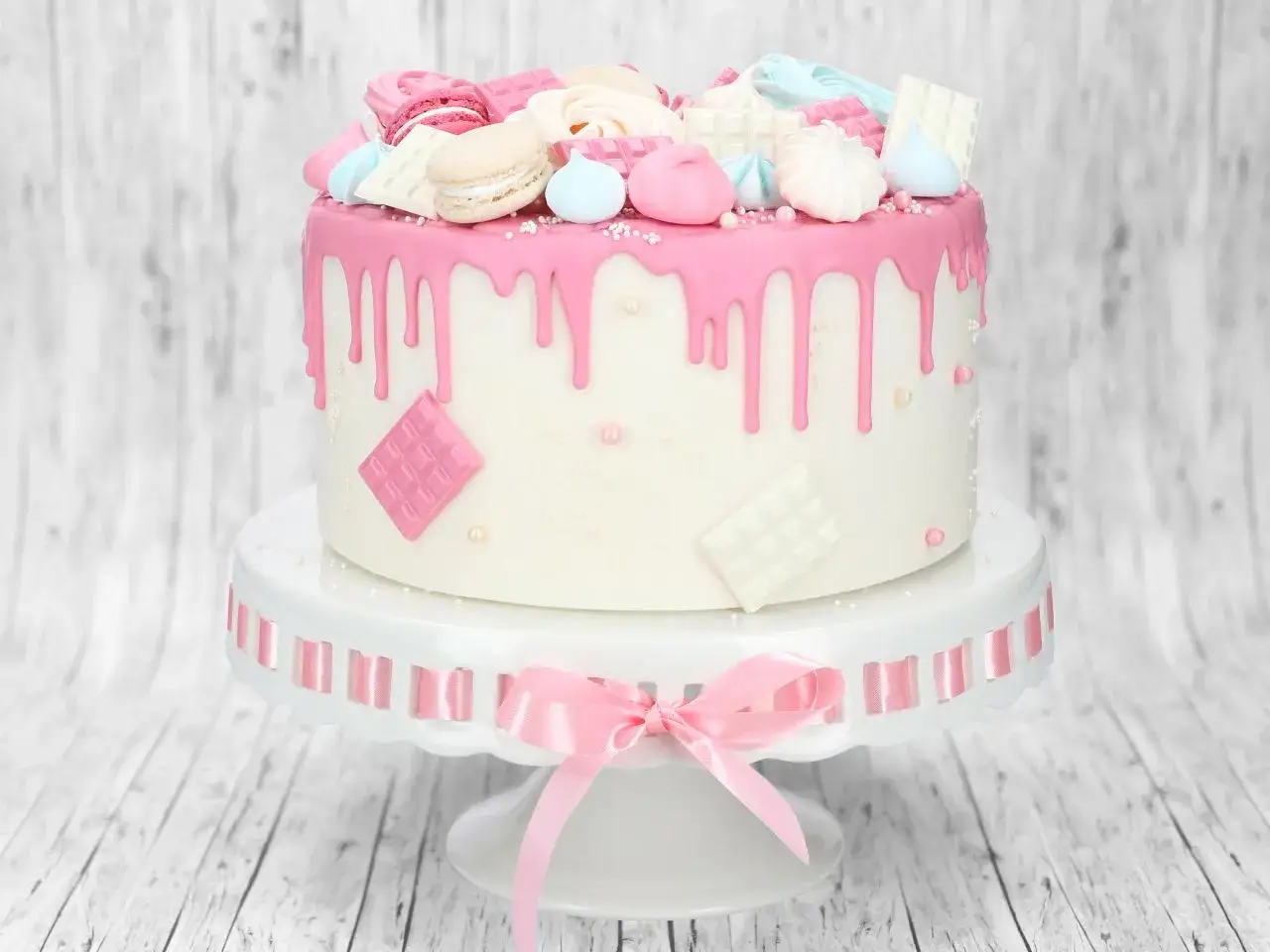 Ein weißer Kuchen mit rosa Zuckerguss-Tropfen, verziert mit Macarons, Meringues und Schokoladenquadraten. Perfekt für ein zuckerguss rezept.