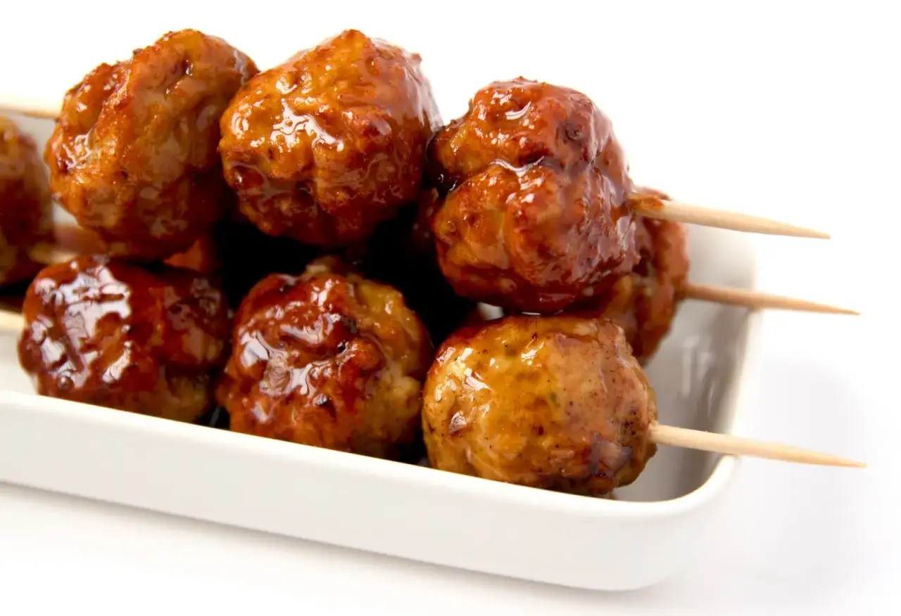 Boulettes de poulet yakitori, napp&eacute;es d'une sauce caram&eacute;lis&eacute;e, servies sur des brochettes en bois dans un plat blanc.