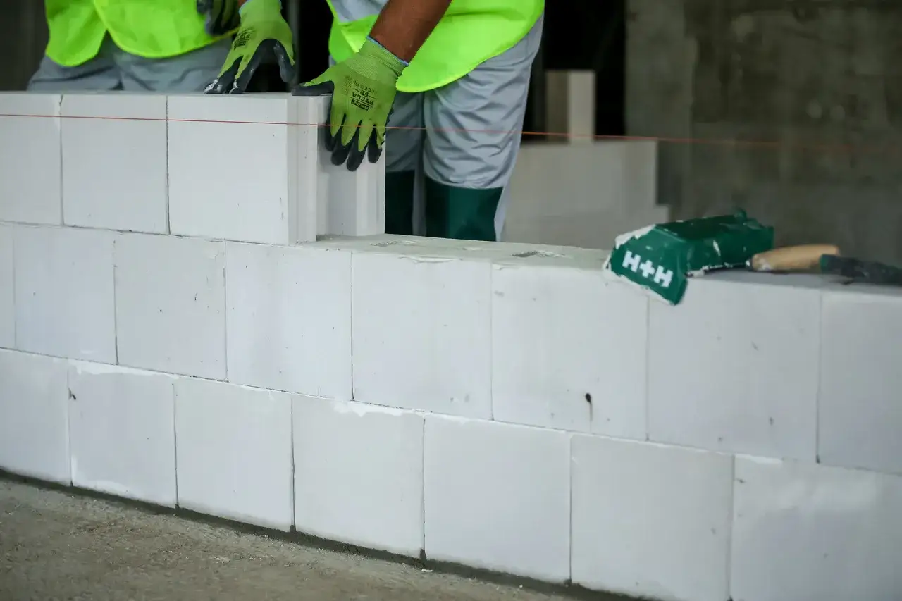 Budowa ściany z bloczków silikatowych. Pracownik w rękawicach zakłada kolejny element.